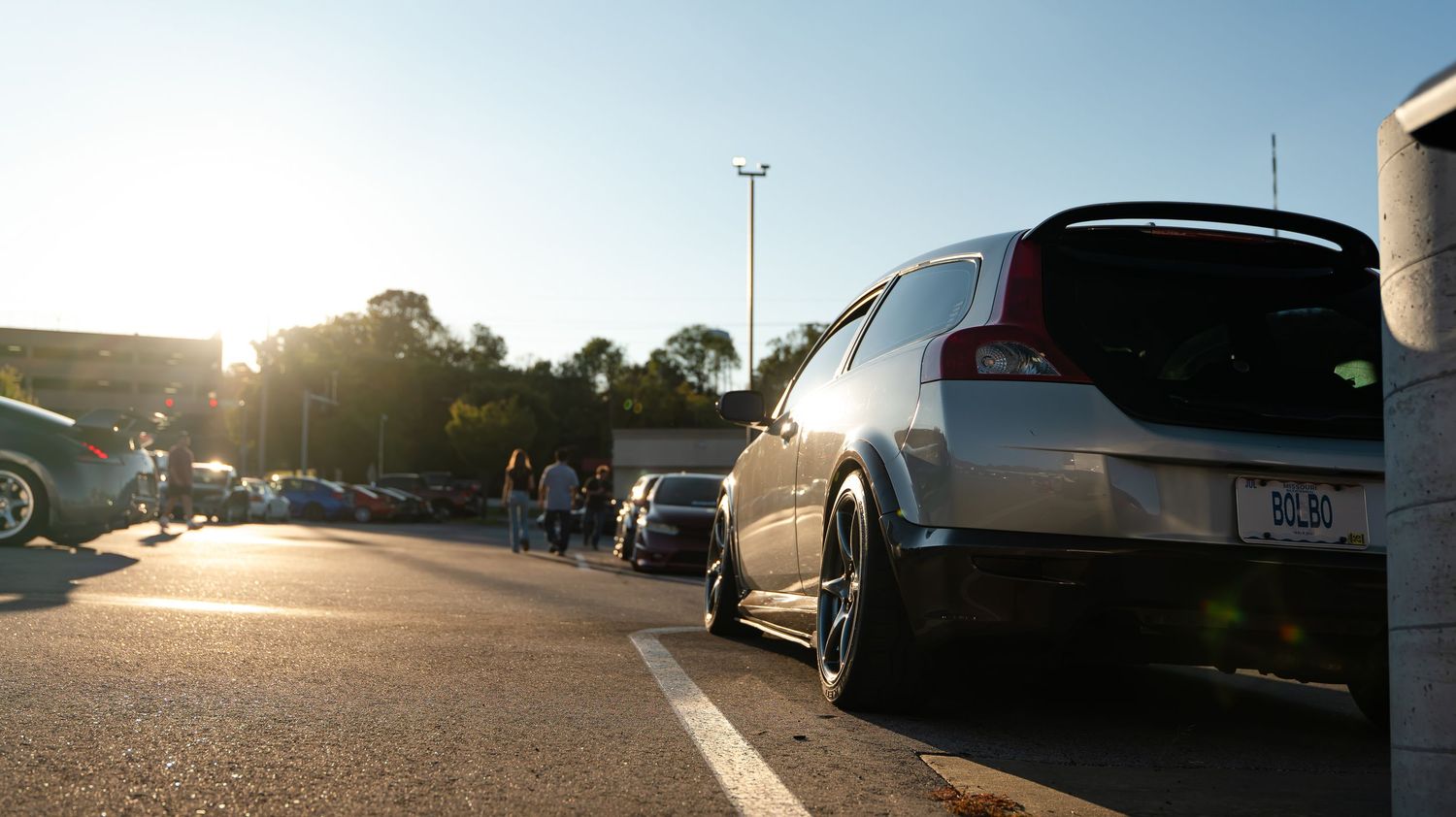 Row of modified cars in a parking lot at sunset.