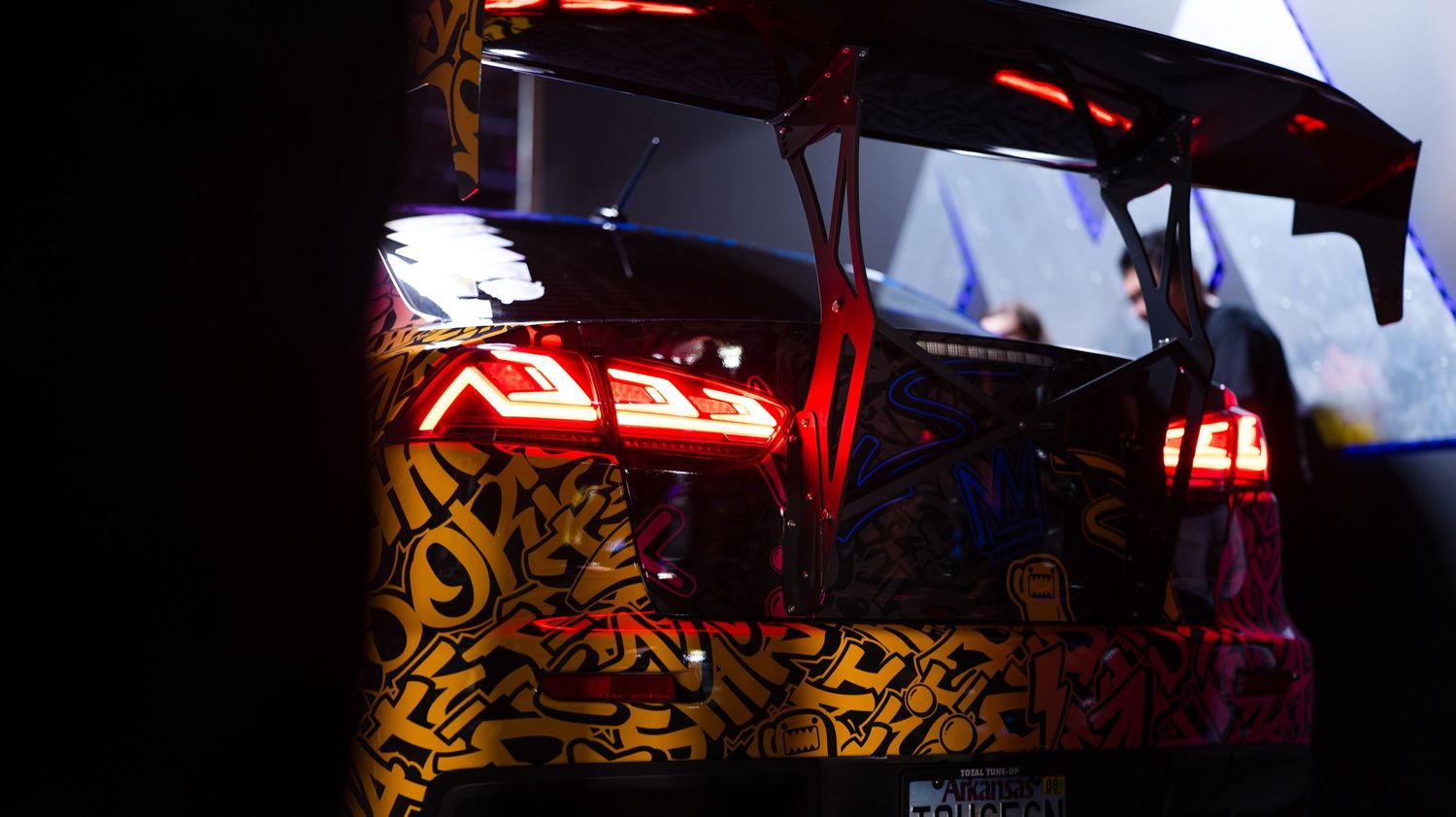 Close-up of custom car with illuminated red LED taillights and decorative patterns.