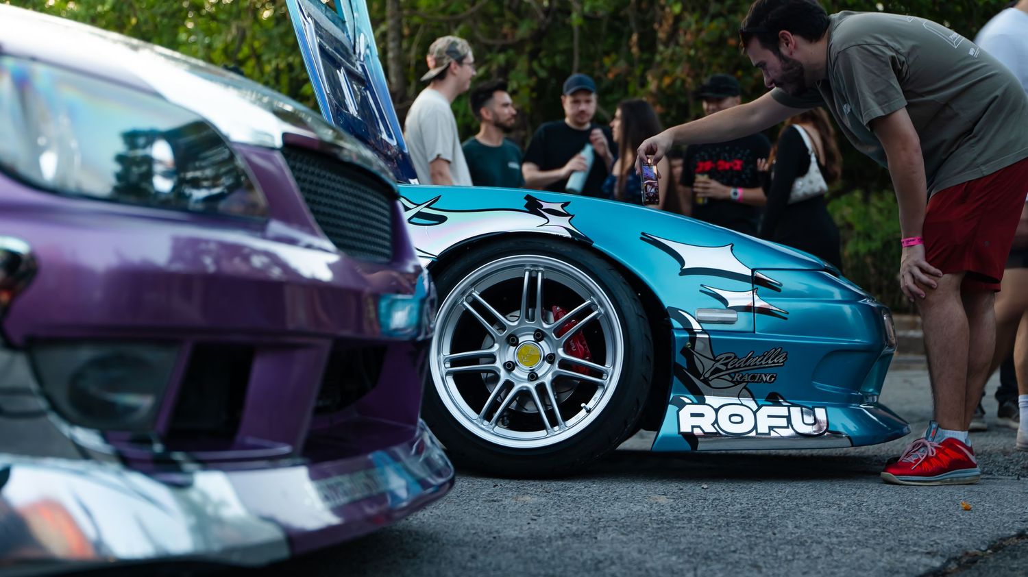 Row of modified sports cars displayed at an outdoor automotive event with spectators.