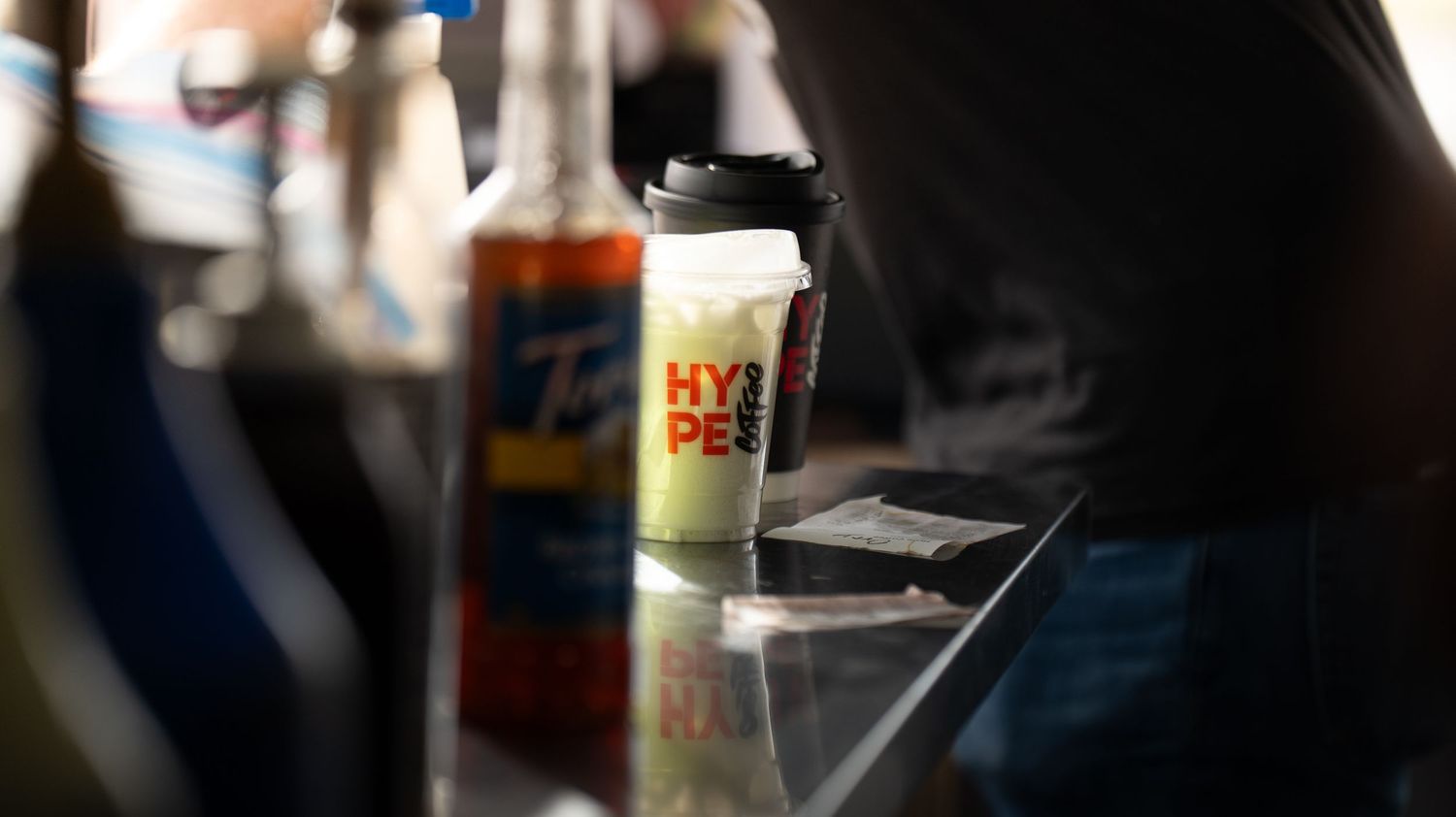 Silhouetted view of people handling drinks and food items at a concession counter.