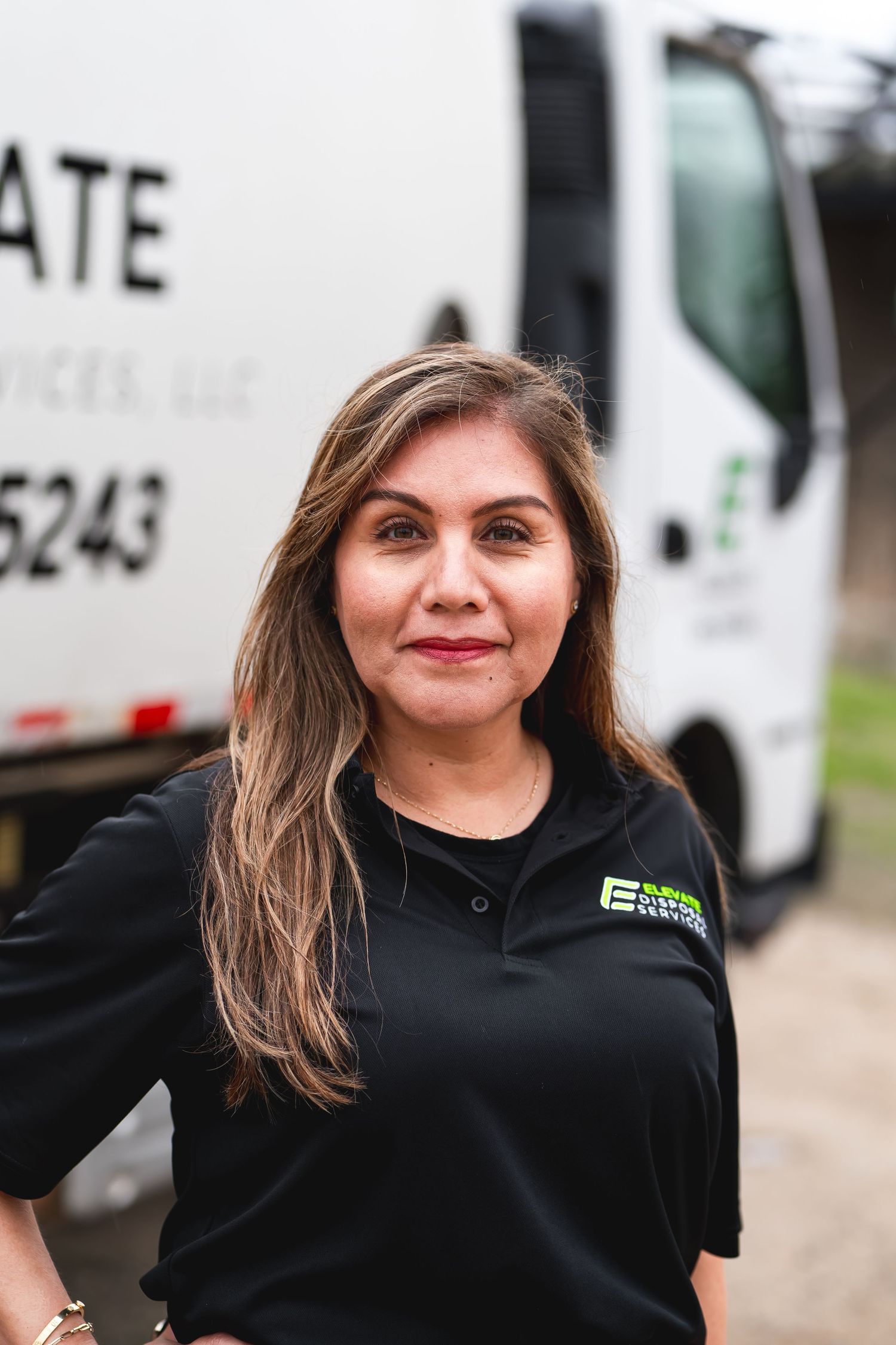 Employee in black polo shirt smiling warmly at the camera in an outdoor setting.