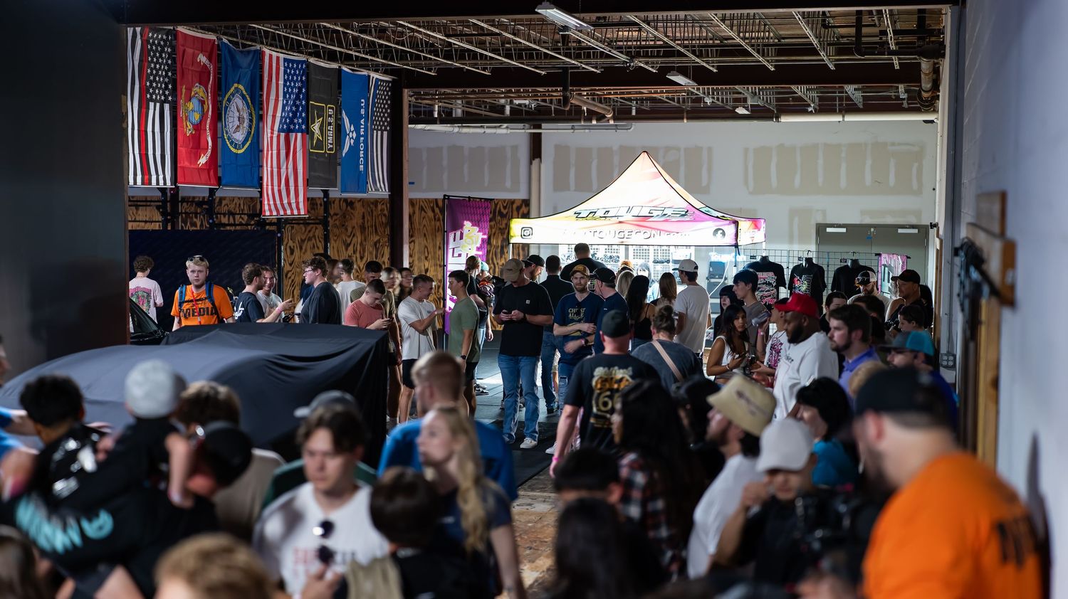 Crowded indoor event space with automotive banners hanging from ceiling.