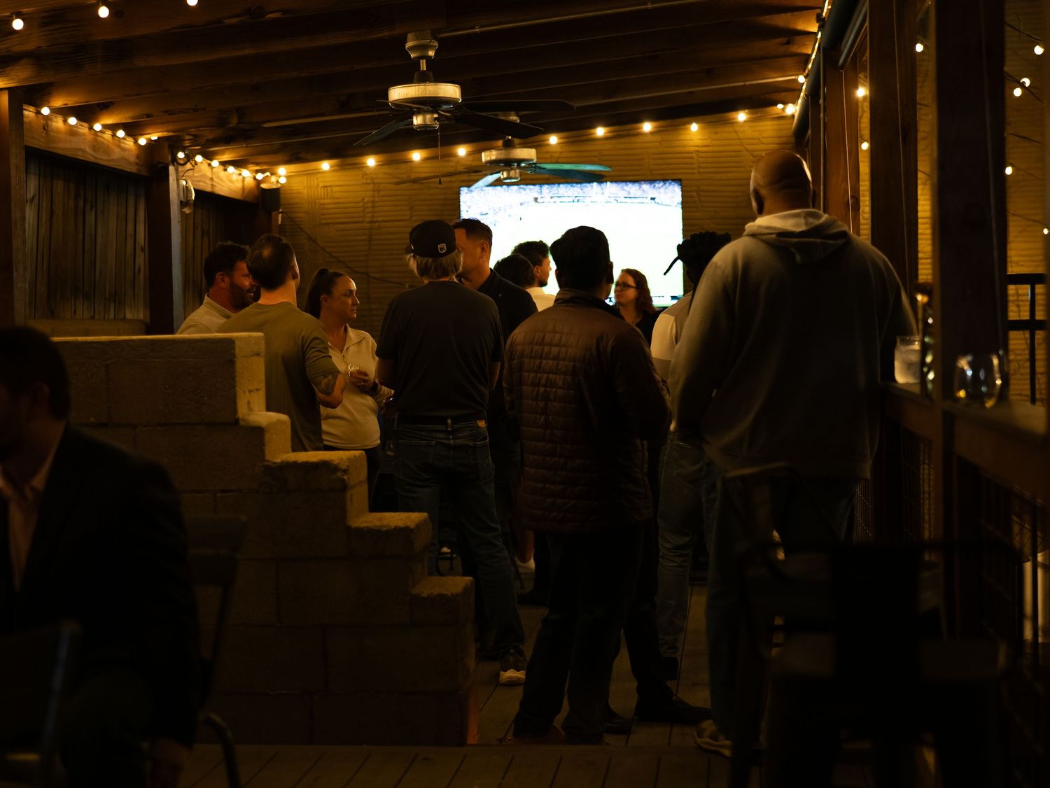 People gather at a dimly lit indoor event space decorated with string lights creating an intimate atmosphere.