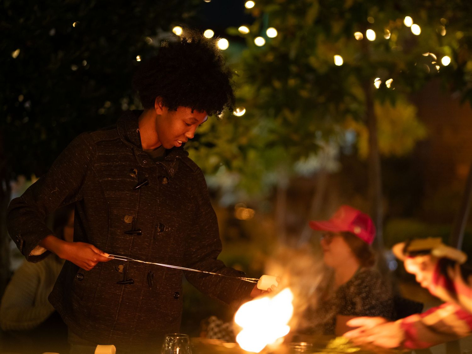 A series of nighttime photos showing people roasting marshmallows over a glowing campfire.