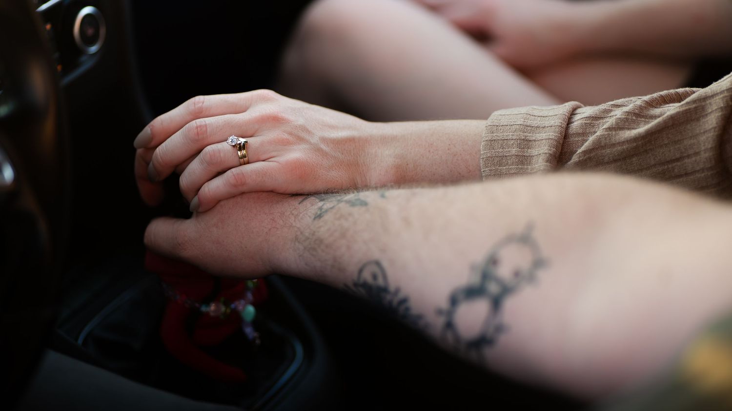 Close-up of tattooed hands resting on car gear shift in natural lighting.