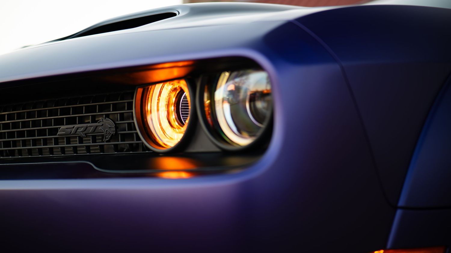 Close-up of modern muscle car headlights glowing in low light conditions.