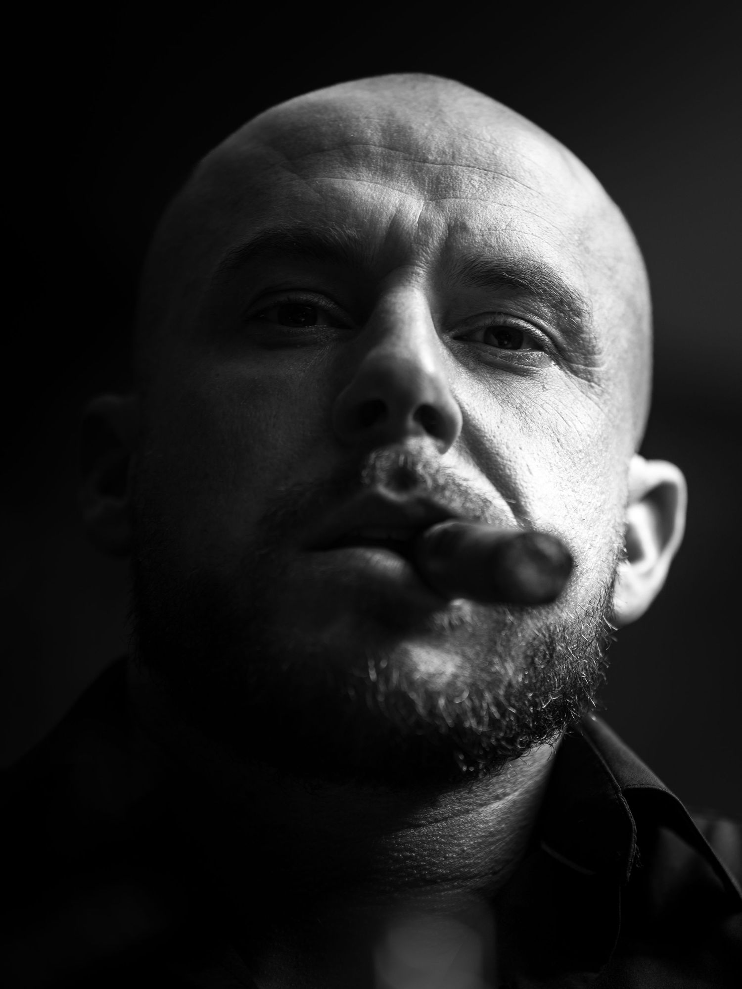 Dramatic black and white portrait of a bald man with a handlebar mustache looking up at the camera.