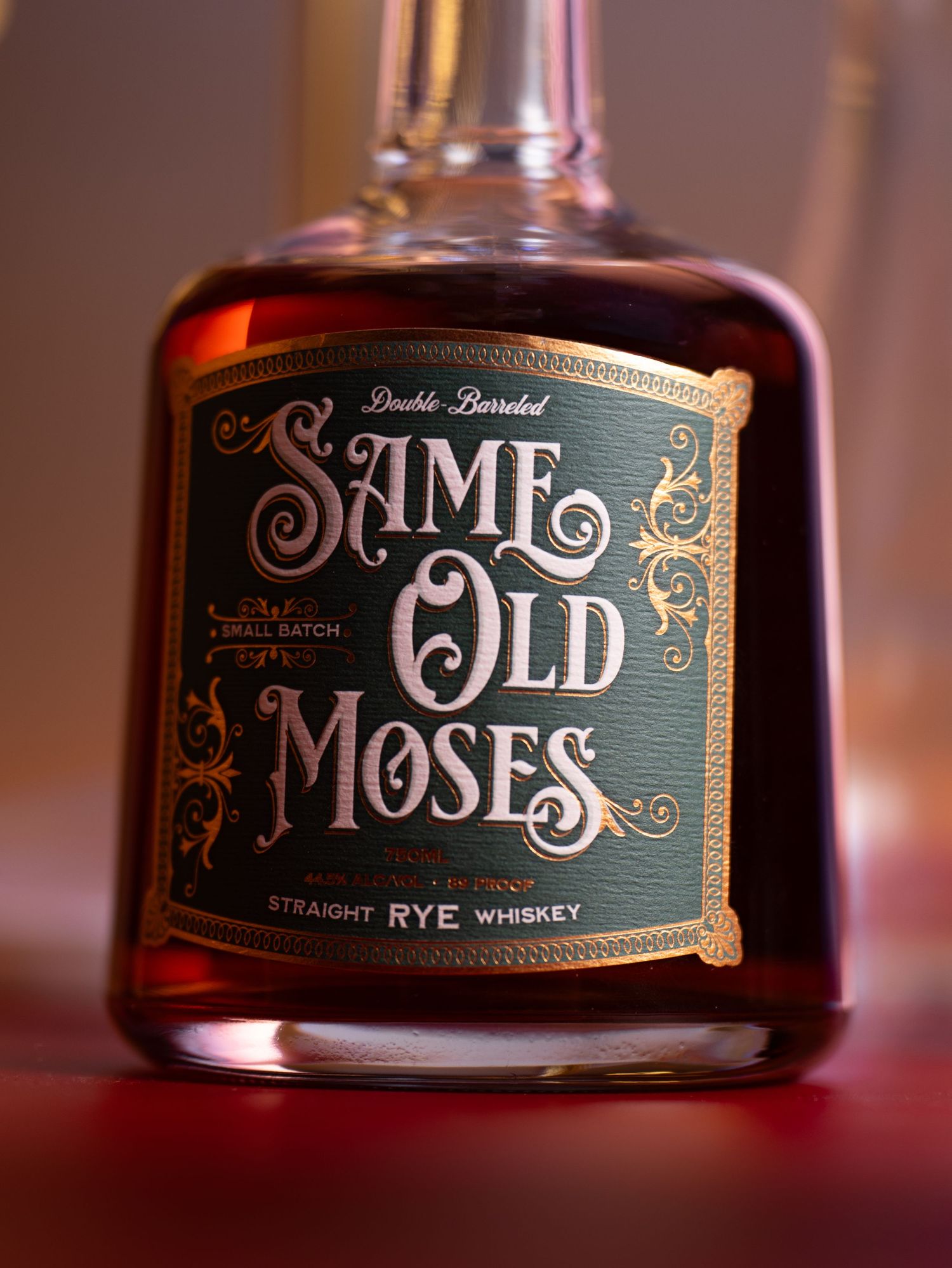 Bottle of Same Old Moses straight rye whiskey photographed against a dark background with red undertones.