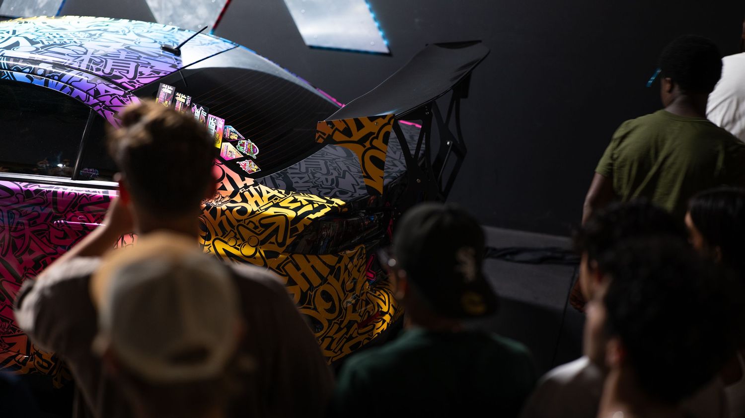 Dark indoor car show with colorful lighting effects and custom vehicles.