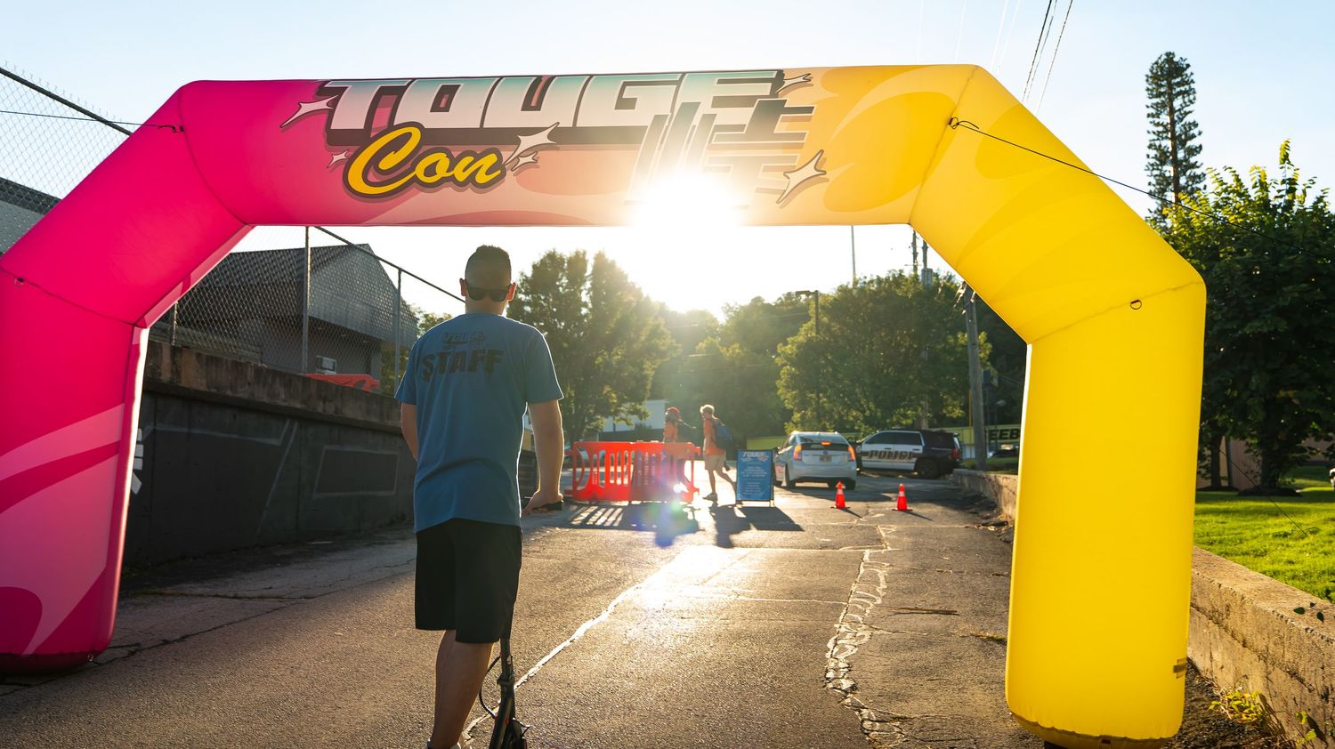 Sunset car meet panorama with pink and yellow entrance arch visible.