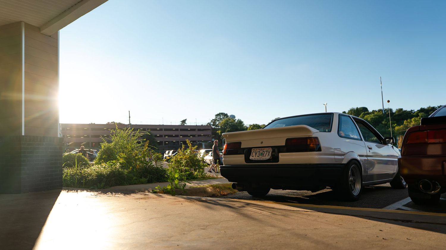 Classic car parked in a lot during golden hour with sun flare.
