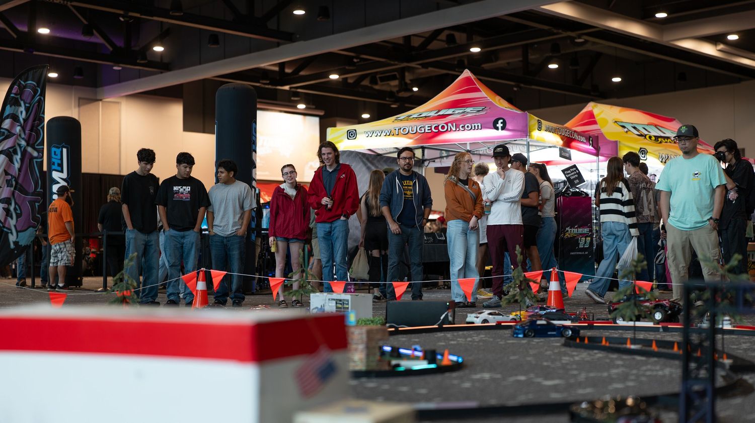 Panoramic view of a crowded indoor car show with multiple vendor booths and displays.