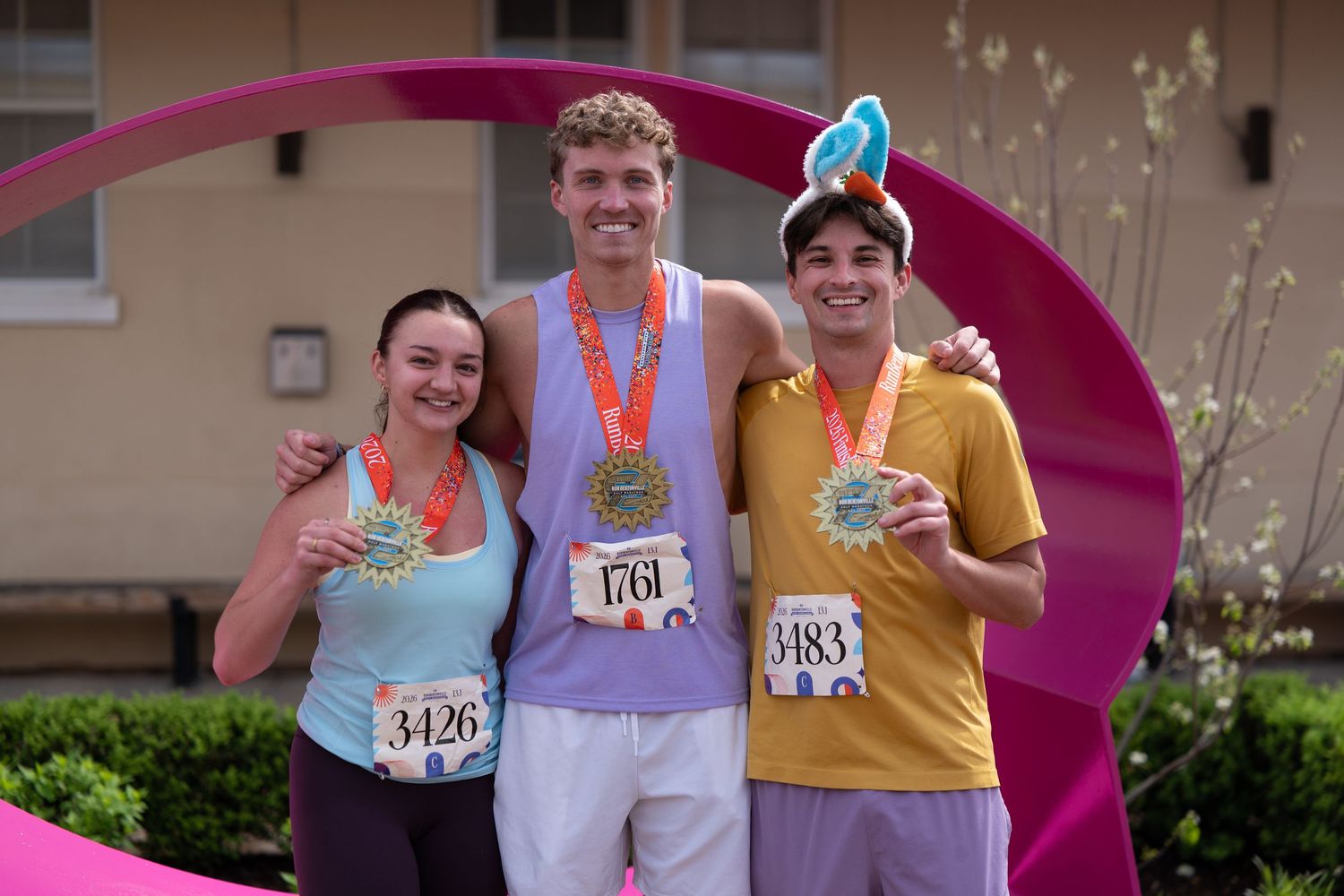 Three smiling race finishers proudly display their medals outdoors after completing a fun run event.