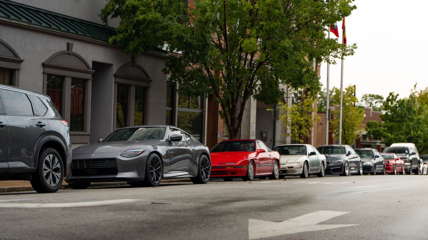 Street view showing parked cars and buildings with trees lining the sidewalk.