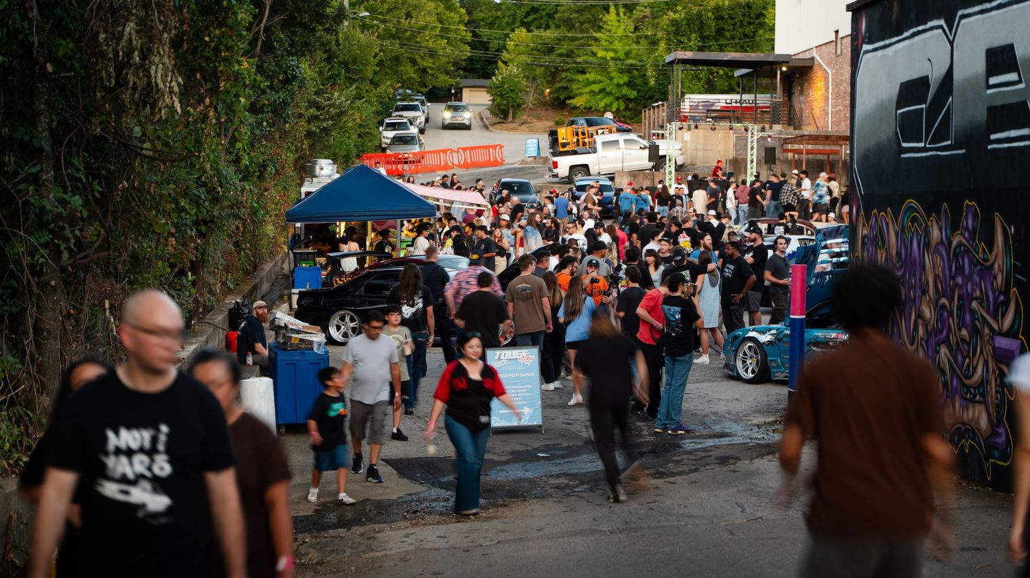 Panoramic view of outdoor event space with trees and crowd in background.
