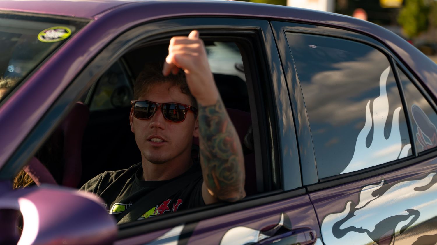 Custom purple car with flame decals parked at automotive event.