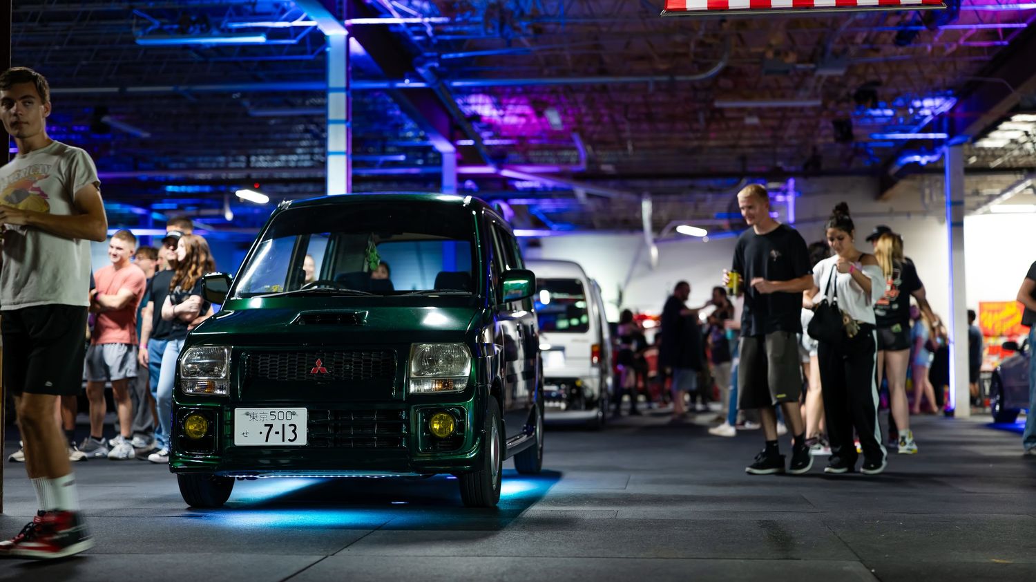 Modified cars displayed in parking structure with blue and red accent lighting.