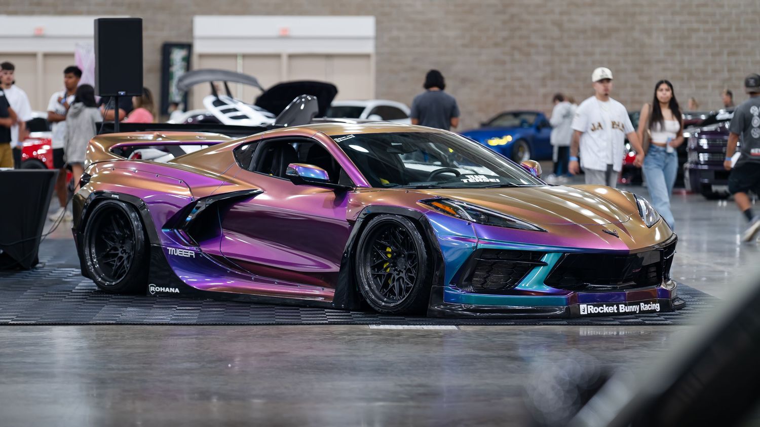 Modified luxury cars on display at an indoor auto show with spectators viewing.