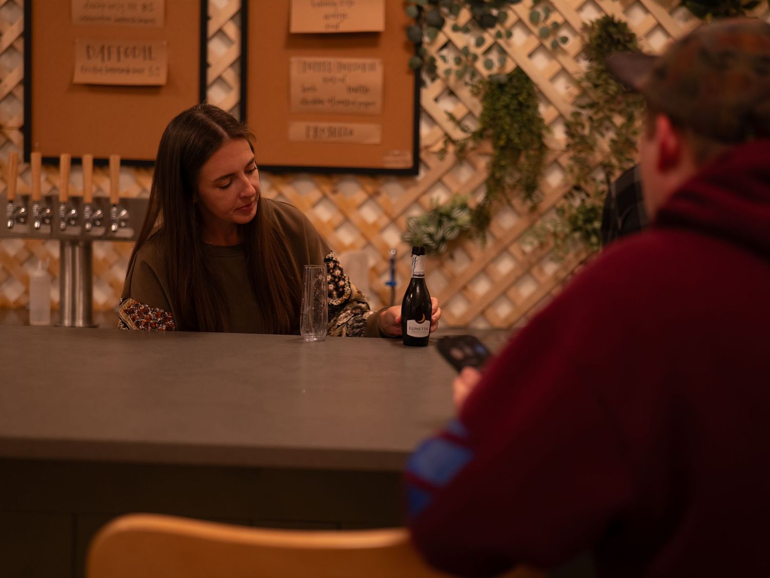 A romantic couple enjoys wine and conversation at a cozy restaurant with warm lighting and framed artwork on the walls.