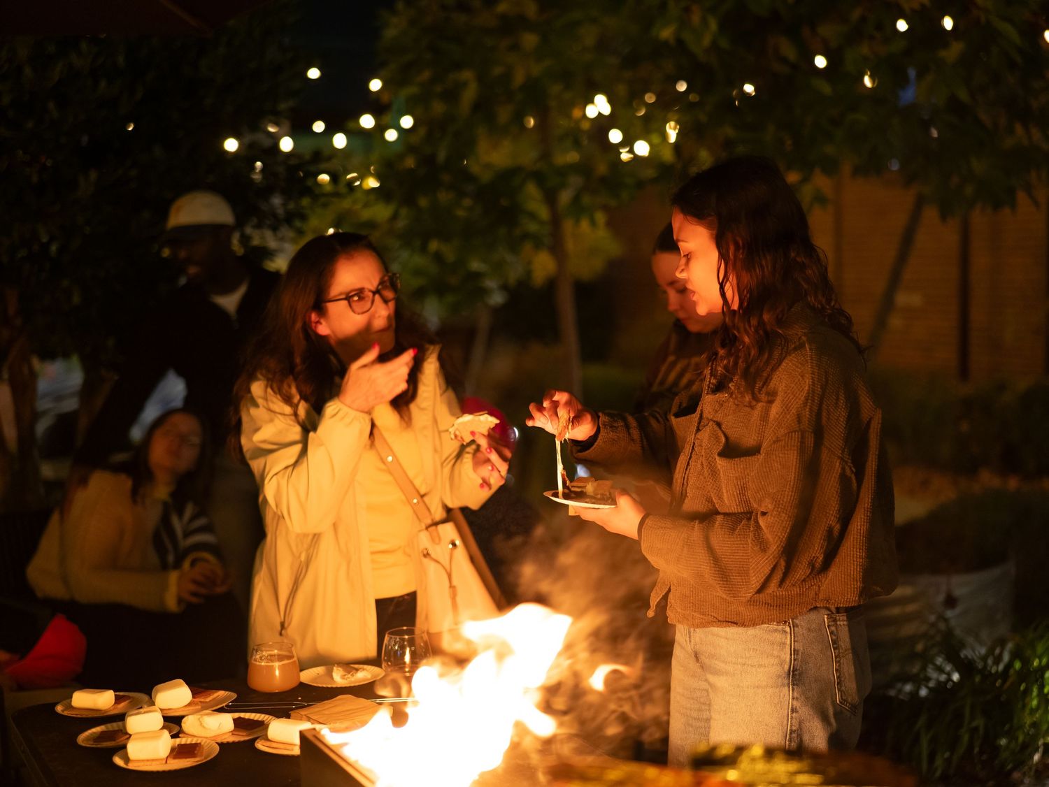 A group of people gather around a fire pit in the evening, creating a cozy outdoor atmosphere.