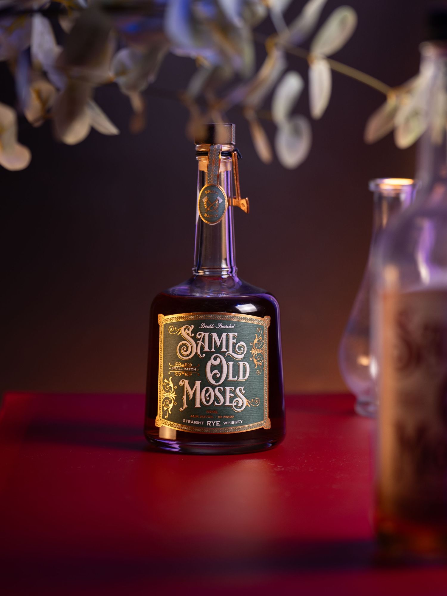 A vintage-style bottle of Saint Old Money liquor sits on a red surface with soft bokeh lighting in the background.