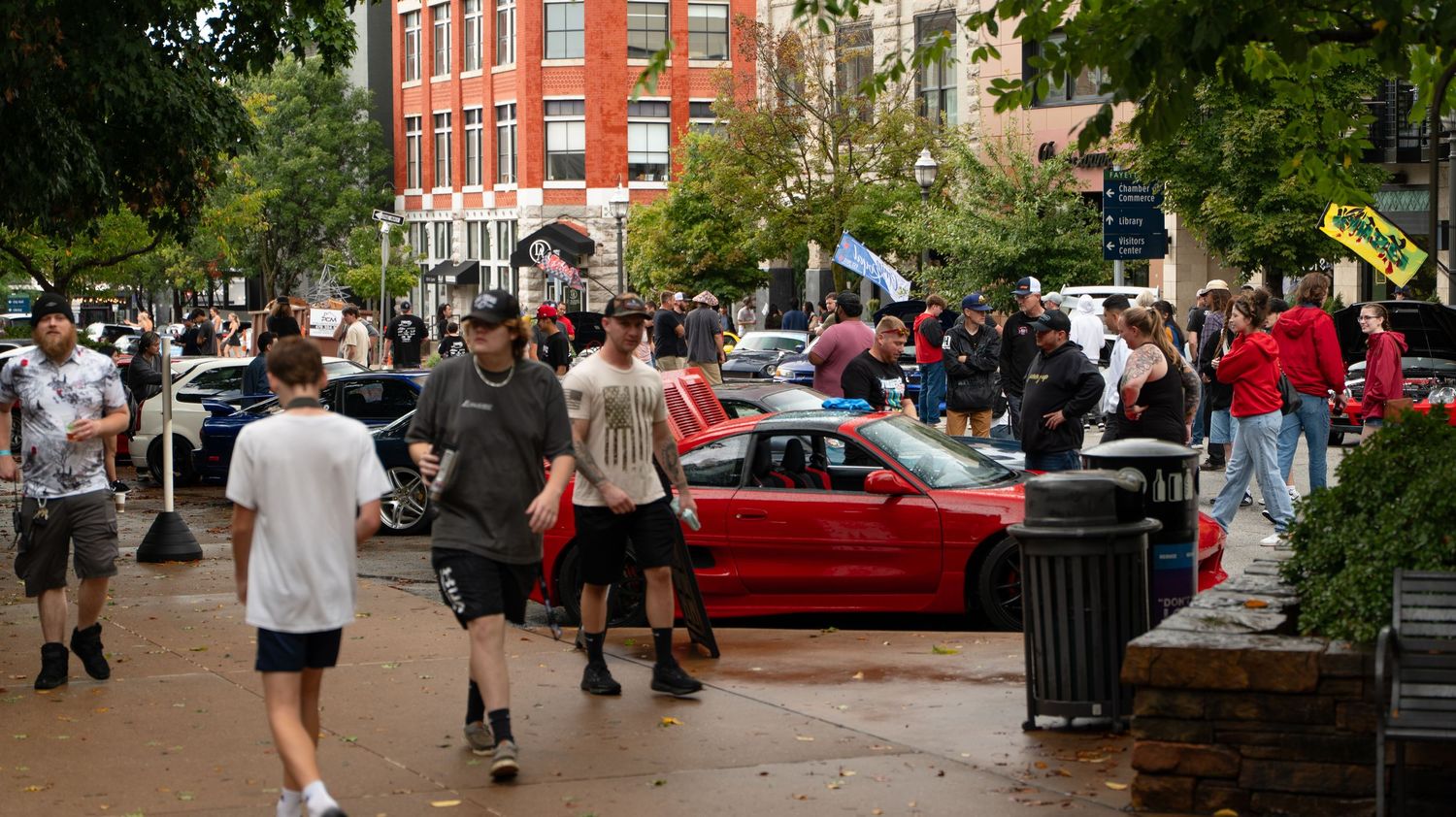Car enthusiasts gathered around vehicles at outdoor street meet.