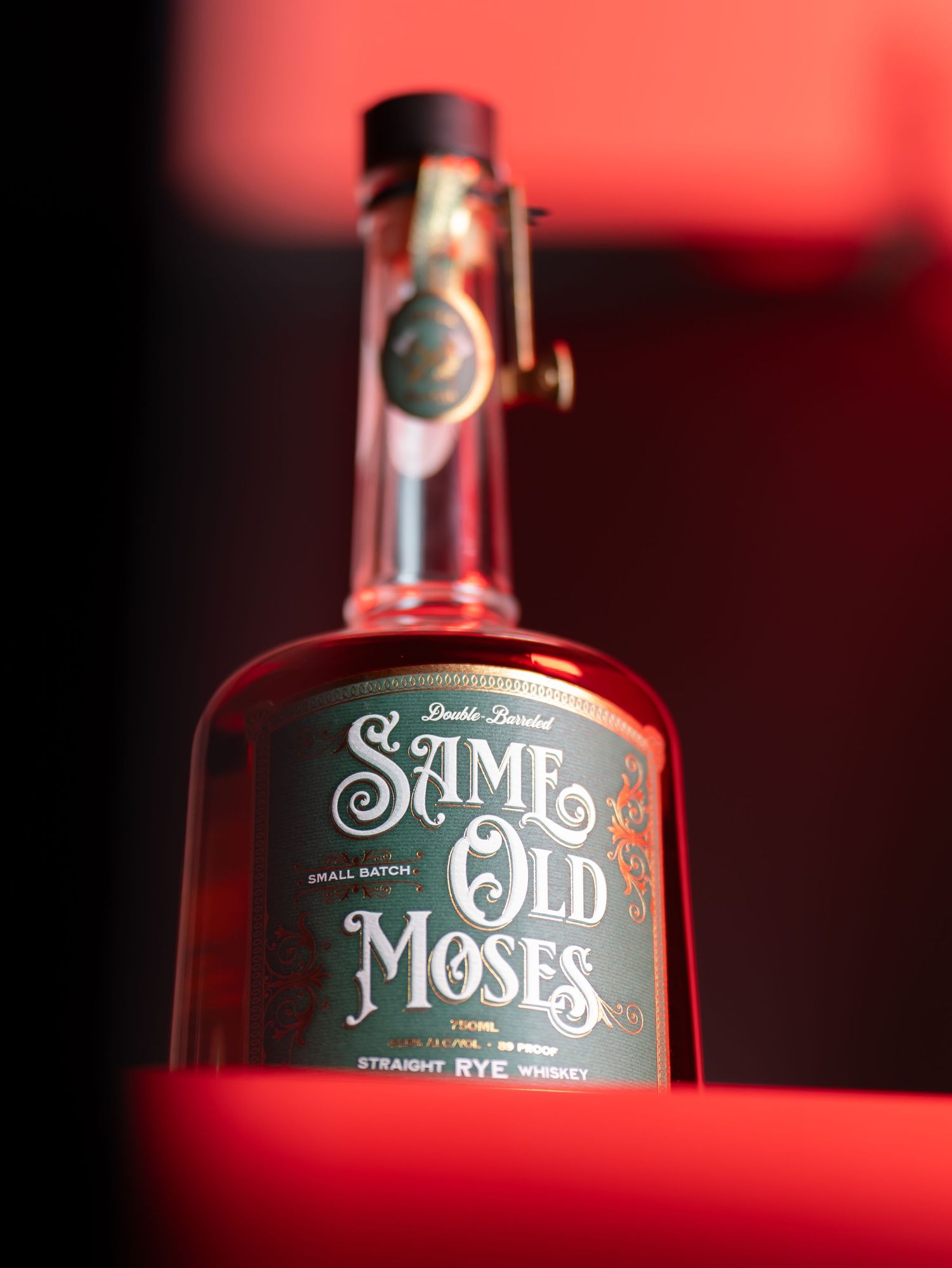 Close-up shots of Same Old Moses whiskey bottle with vintage-style typography against a dark red background.