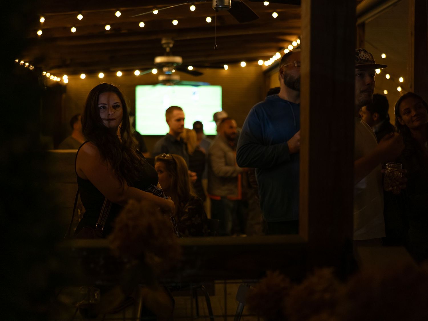 String lights illuminate a dimly lit bar interior with patrons seated at tables and along the counter.