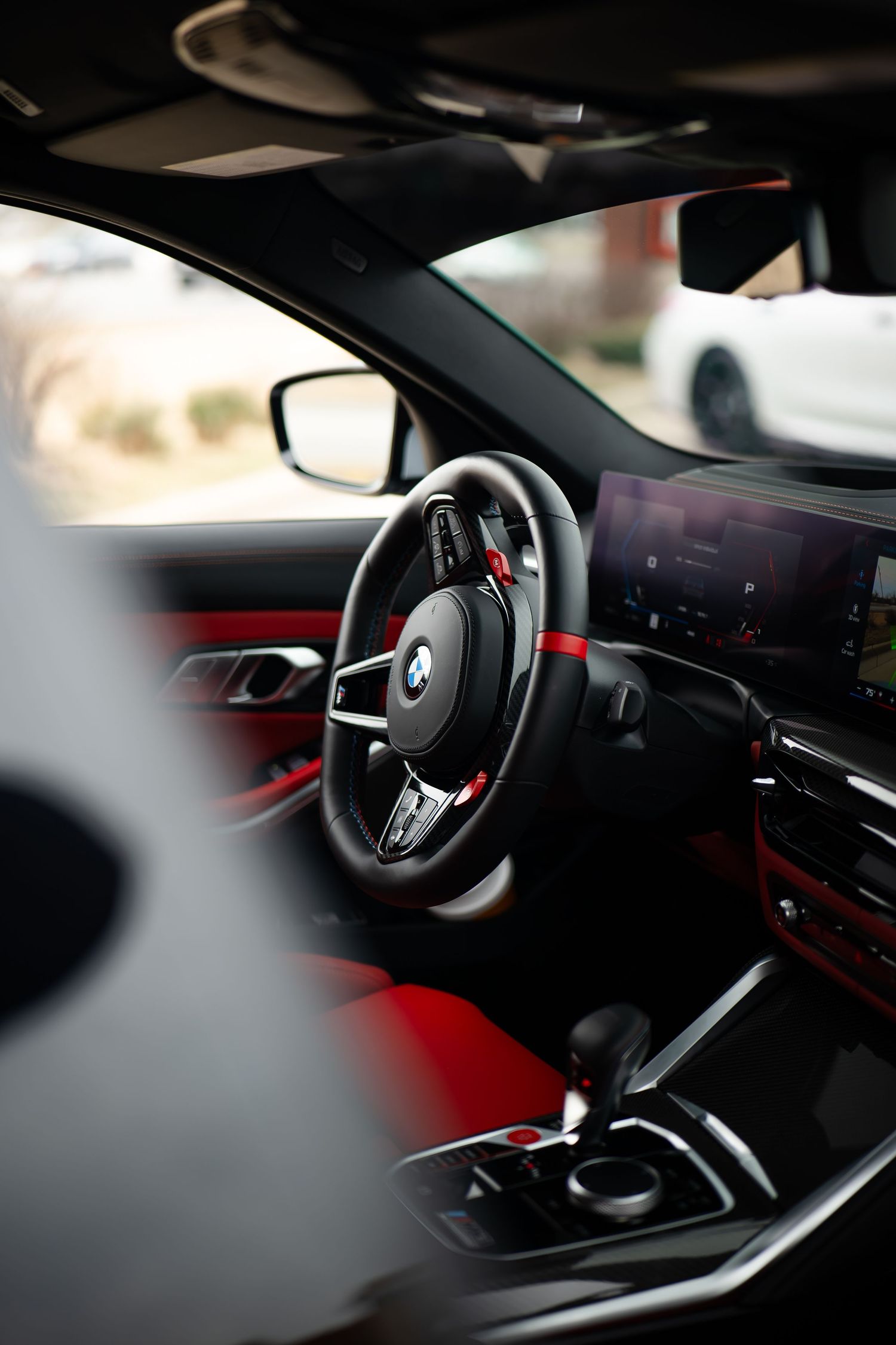 BMW cockpit view showing steering wheel, digital dashboard and red ambient lighting.