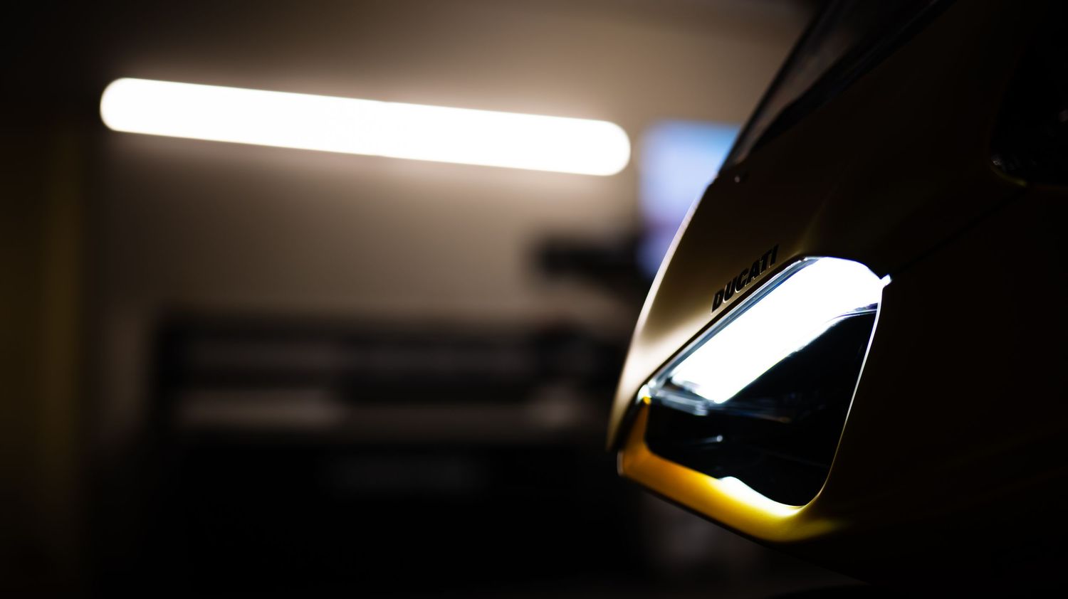 Silhouetted motorcycle parts against bright fluorescent lighting in a garage.
