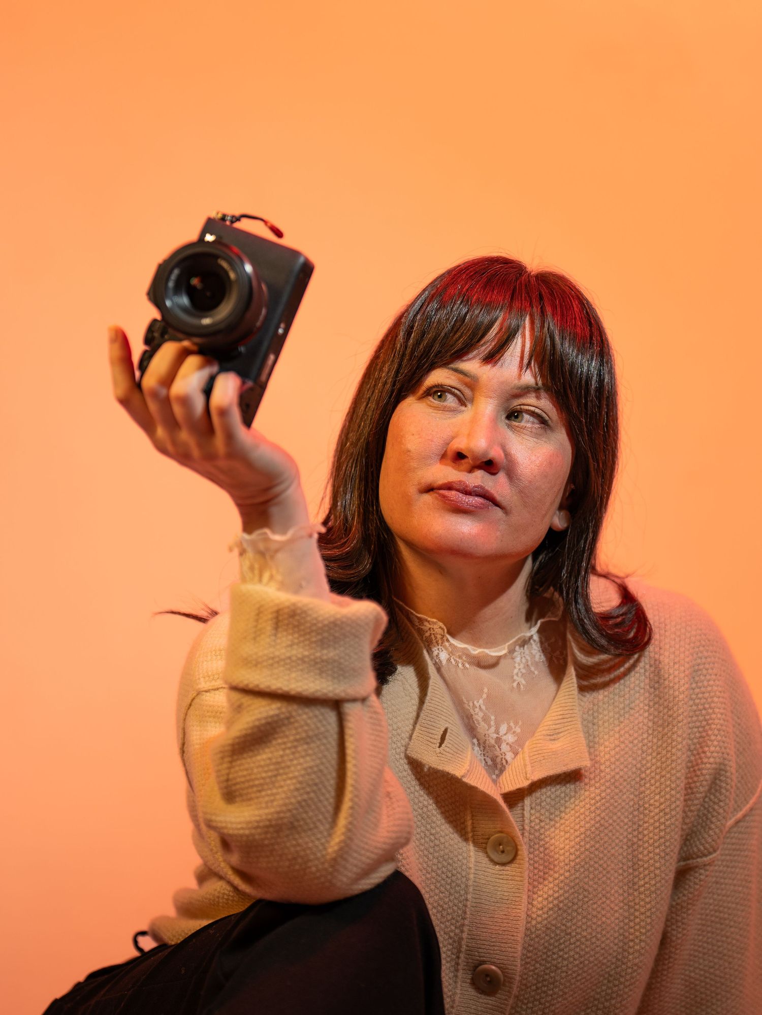 A person in a beige coat poses with a camera against an orange background in a sequence of four photos.