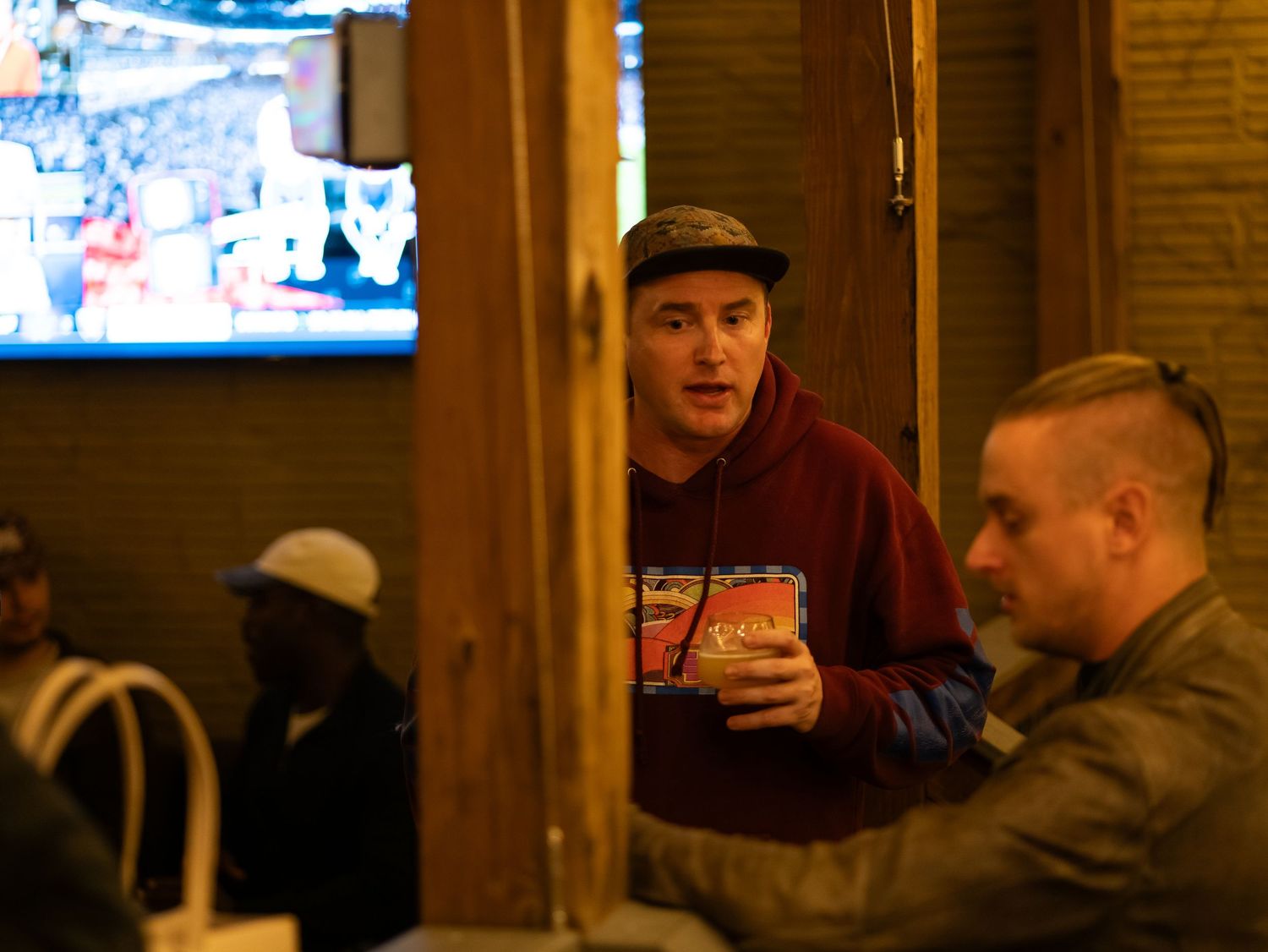 People gather at a rustic wooden bar counter inside a cozy pub or restaurant.