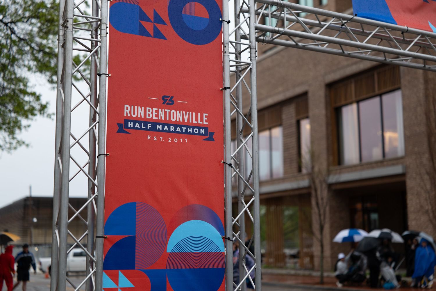 Run Bentonville Half Marathon sign displayed on a metal truss frame outdoors on a rainy day.