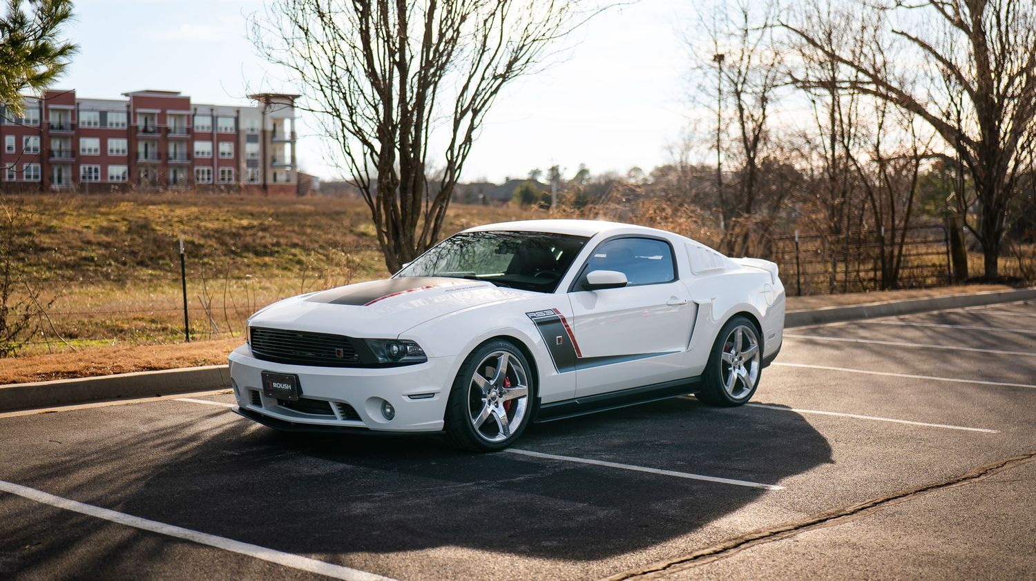 Panoramic view of modified cars parked in front of bare trees and brick buildings.