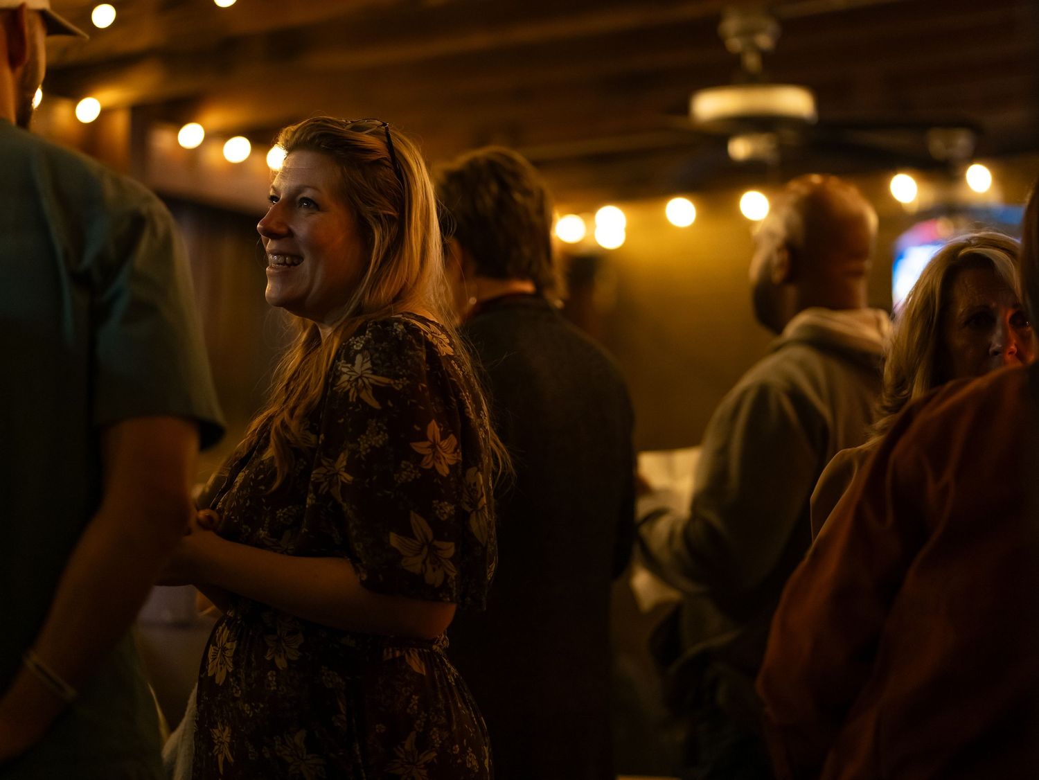 People dancing and celebrating at a dimly lit wedding reception with string lights overhead.