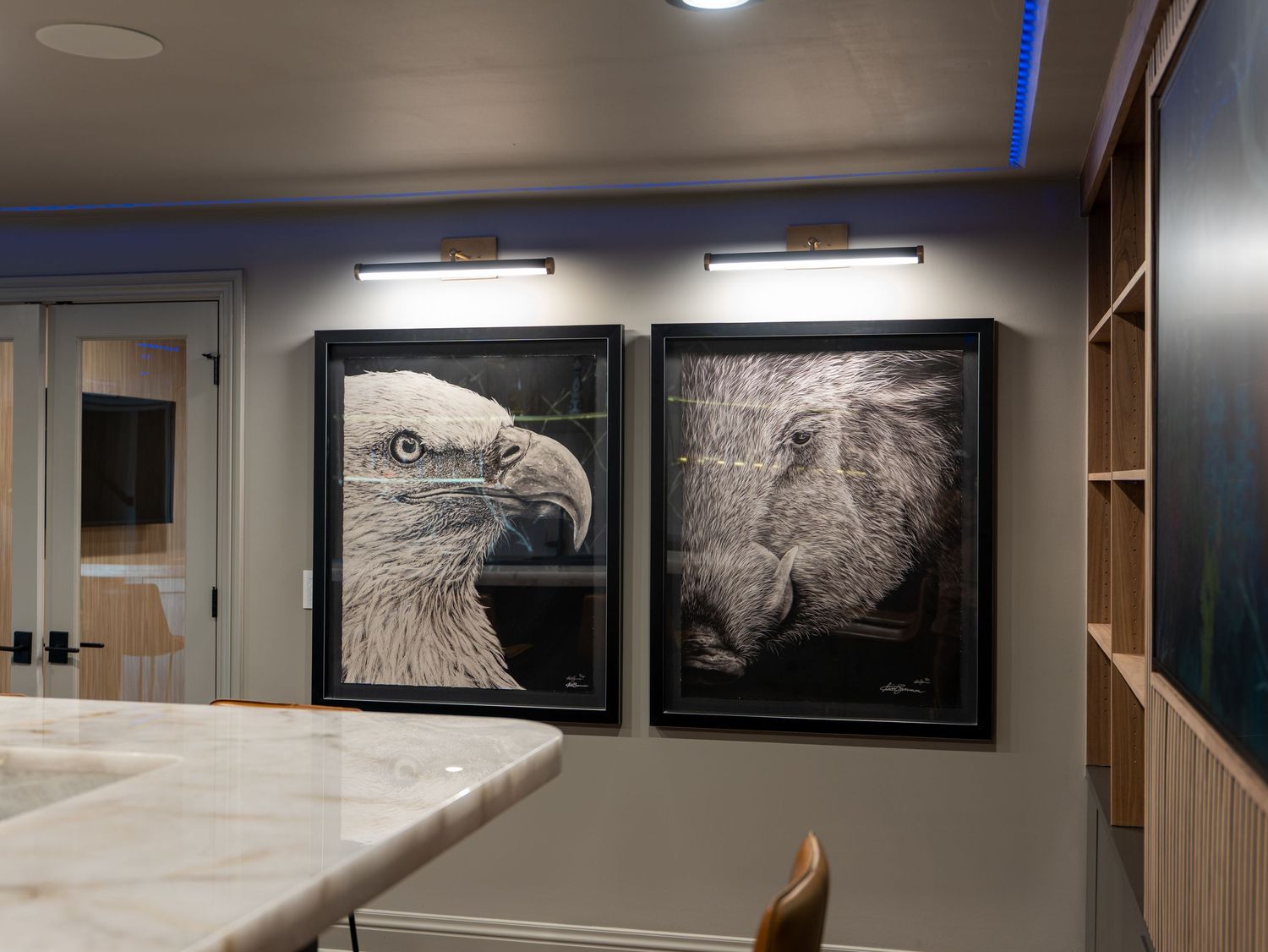 Two large framed black and white eagle artwork prints displayed on a gray wall with accent lighting above them.