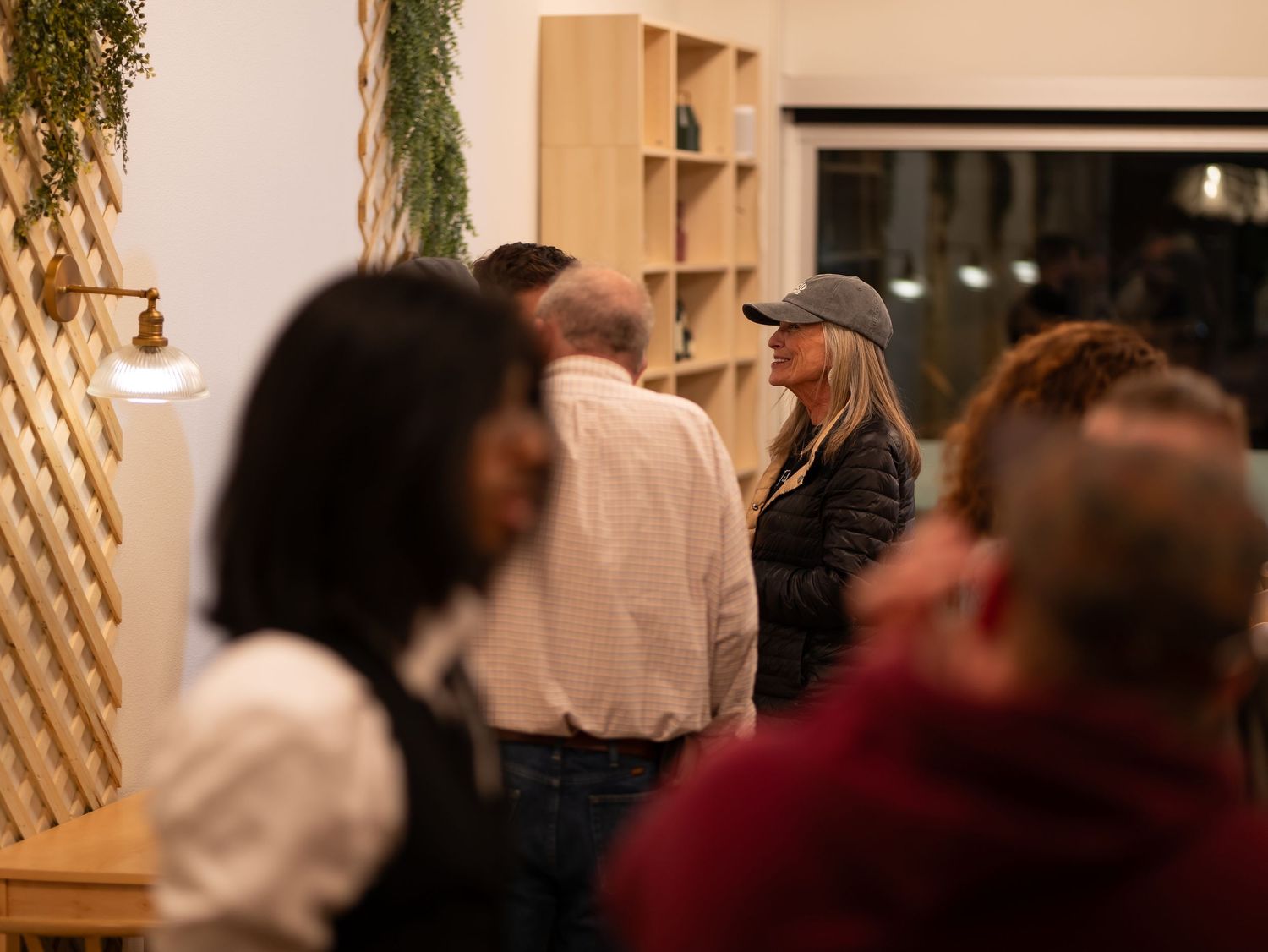 People gather in a warmly lit restaurant interior with wooden shelving and decor visible in the background.