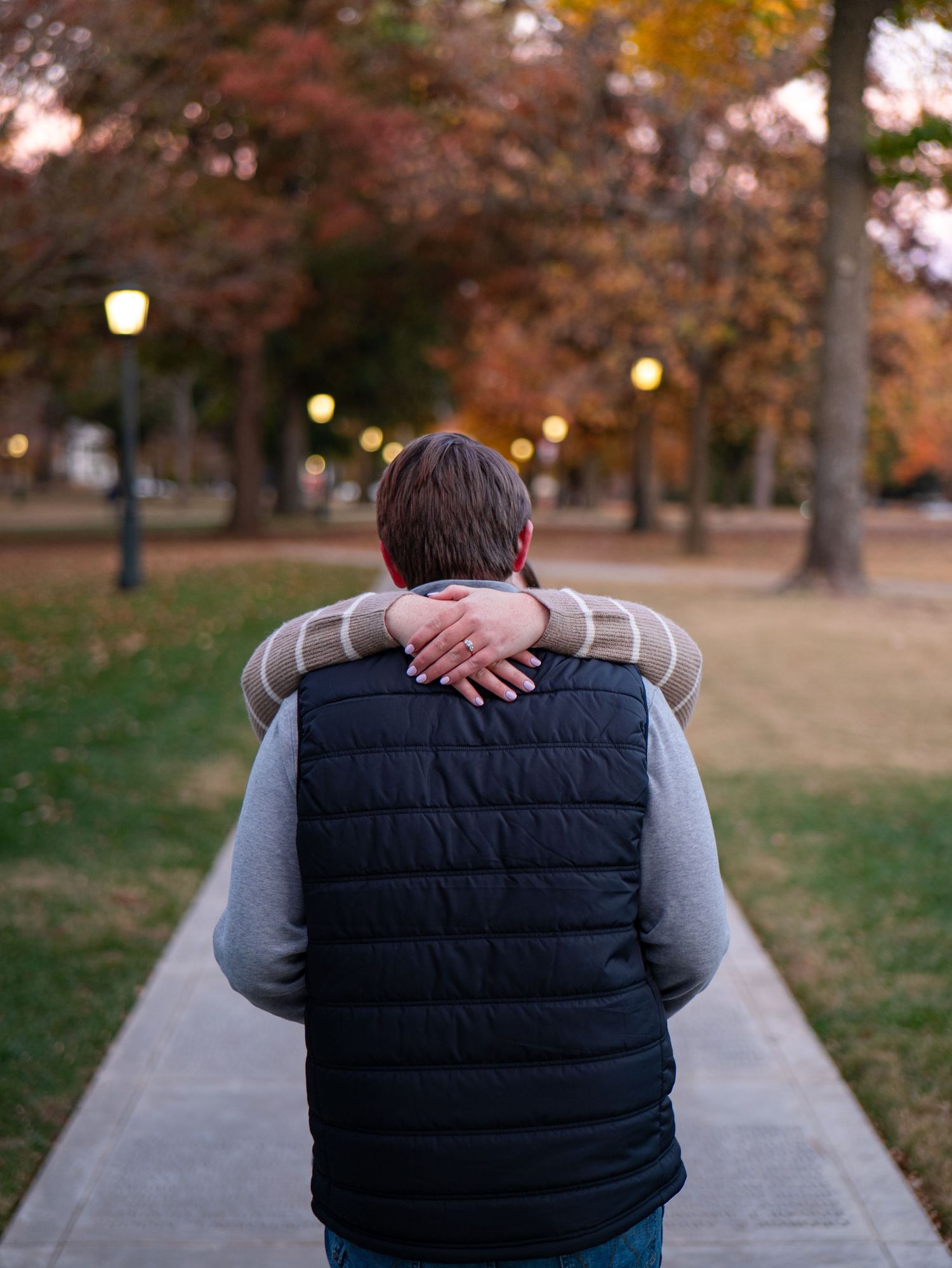 A couple embraces while sitting on a bench surrounded by autumn trees with warm lighting at dusk.