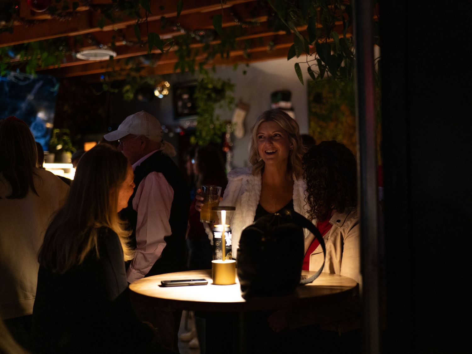People mingle at a dimly lit evening social gathering with warm ambient lighting.
