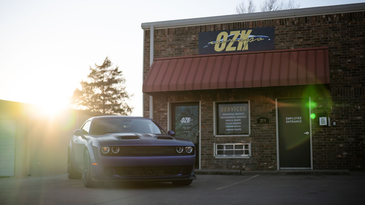 Purple Dodge Challenger parked outside a brick building at sunset.