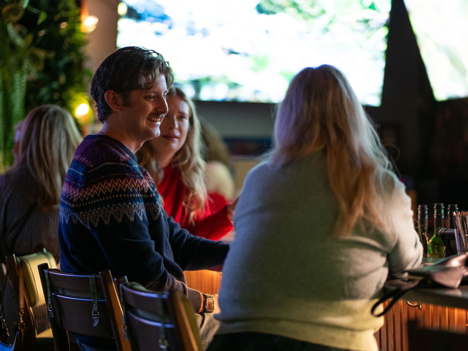 People enjoying drinks and conversation at a dimly lit bar with warm ambient lighting.
