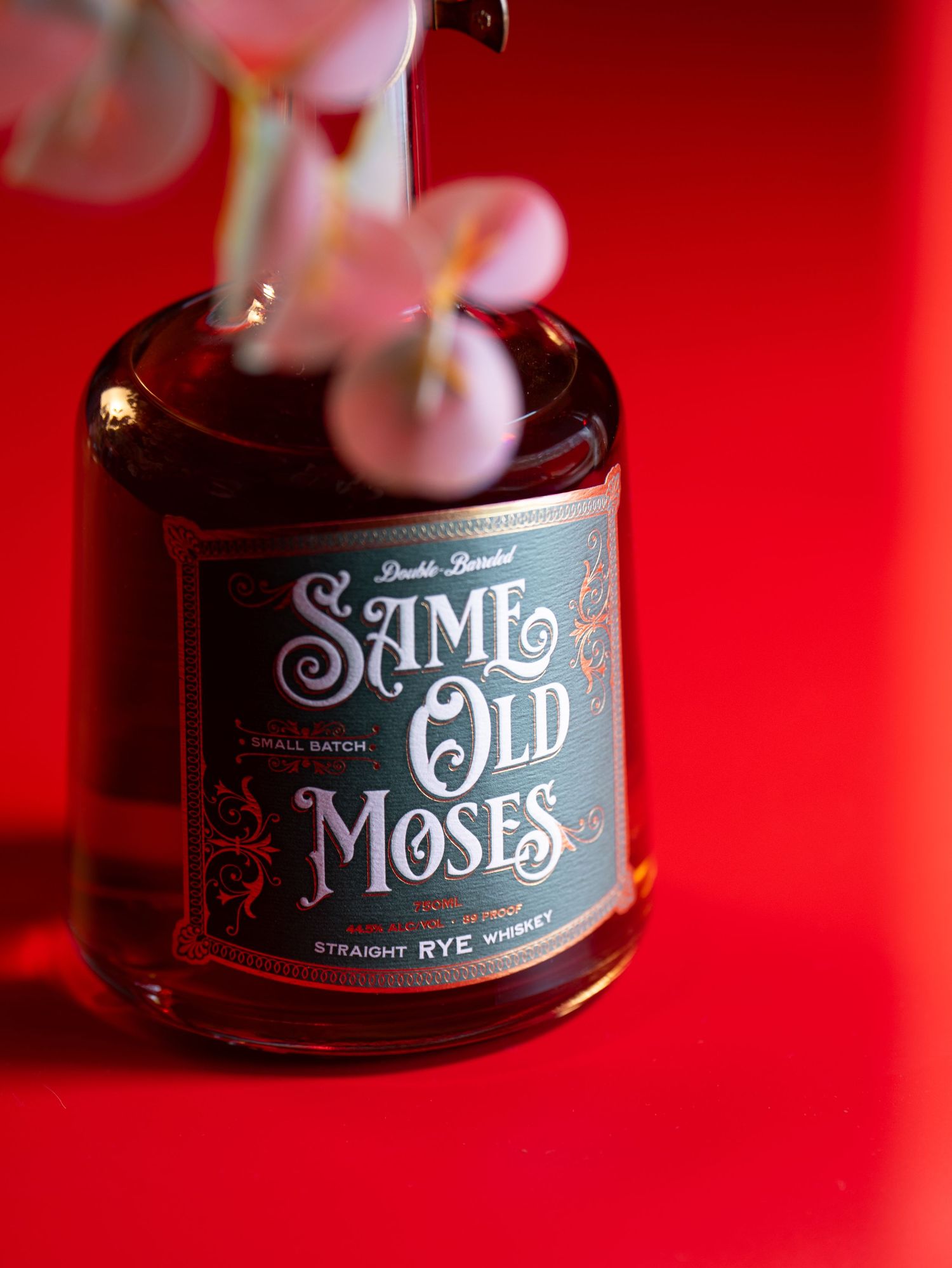 A bottle of Saint Moses rye whiskey with ornate black and gold label design against a vibrant red background.