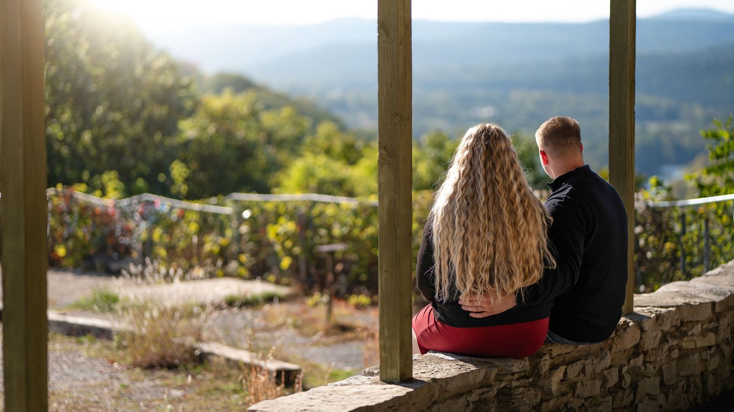 Panoramic mountain view through wooden deck posts with people enjoying the scenery.
