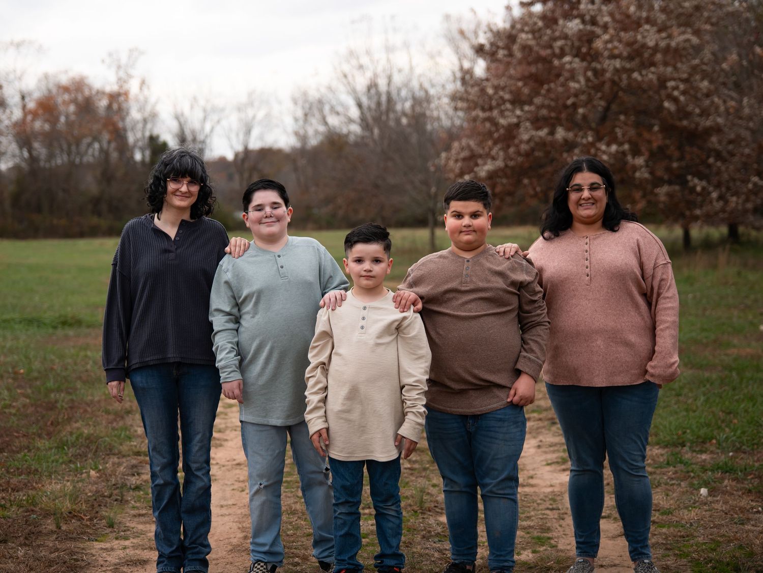 A family group wearing coordinated neutral tones poses together in an autumn field setting.