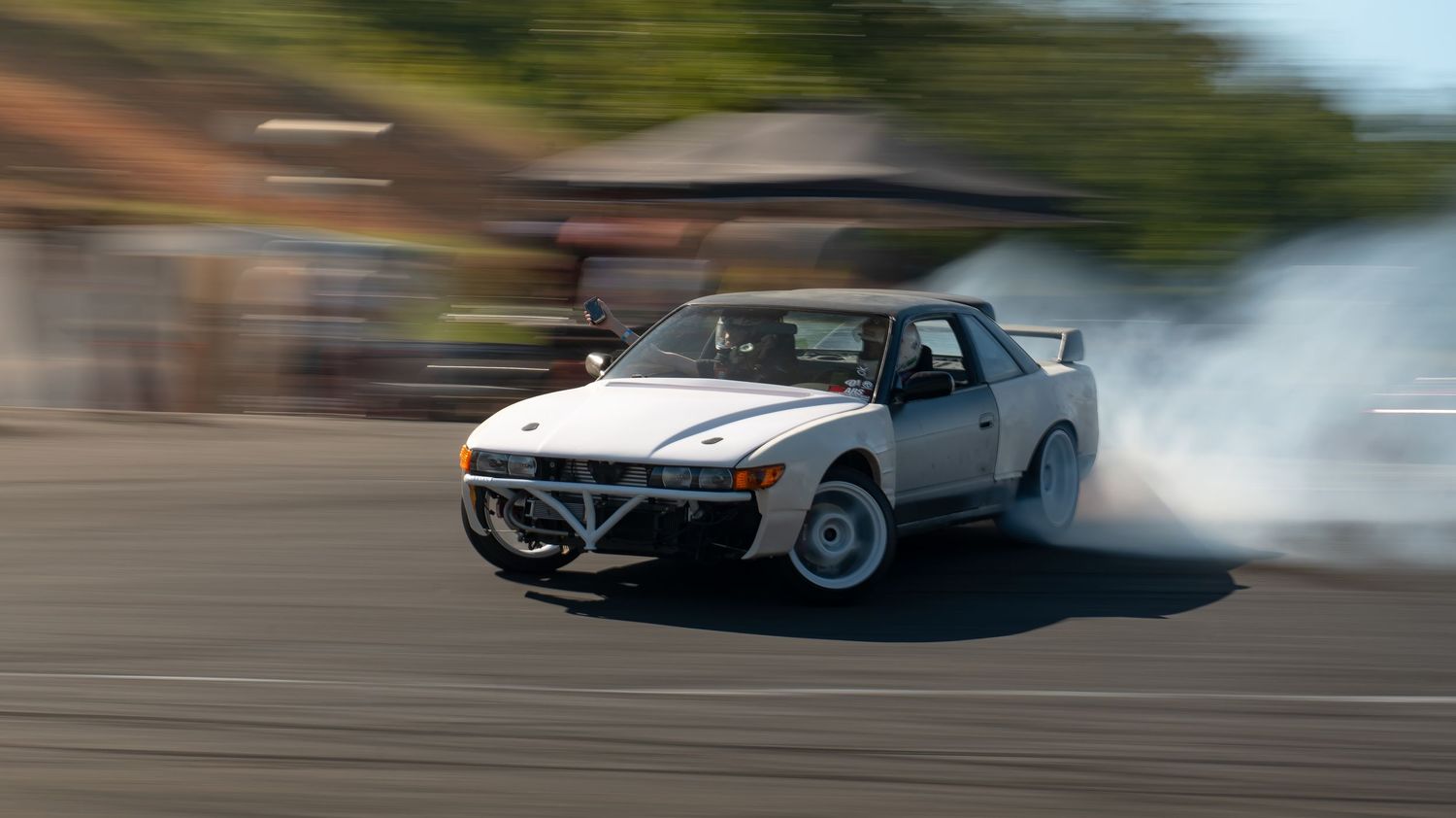 Fast-moving cars creating motion blur effect during daytime drifting event.