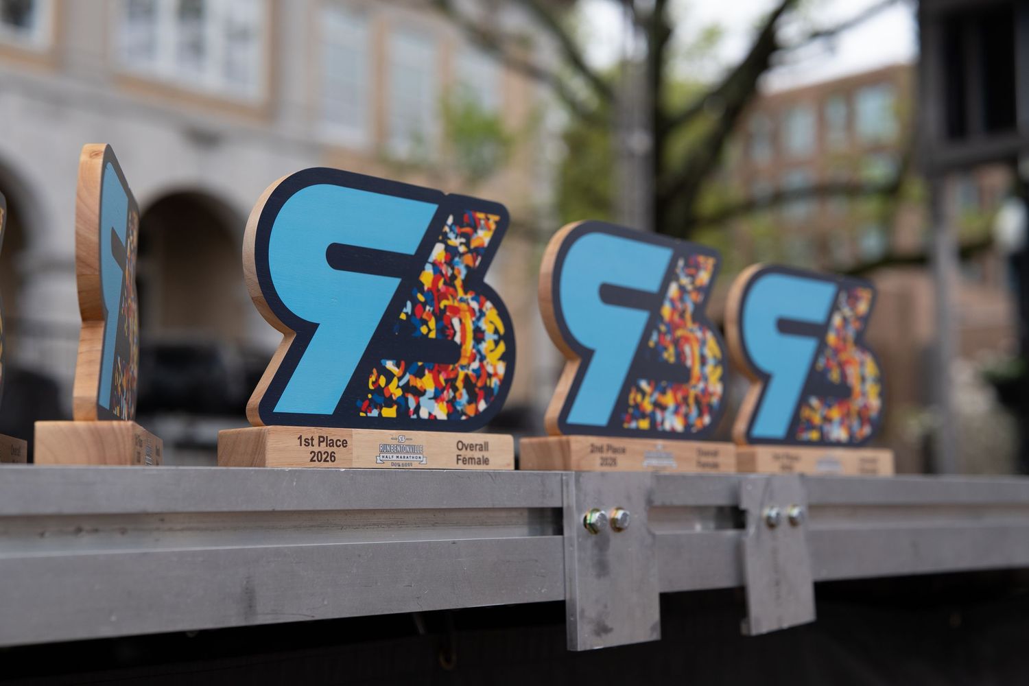 Colorful trophy awards with blue letter R design on wooden bases displayed on a table outdoors.