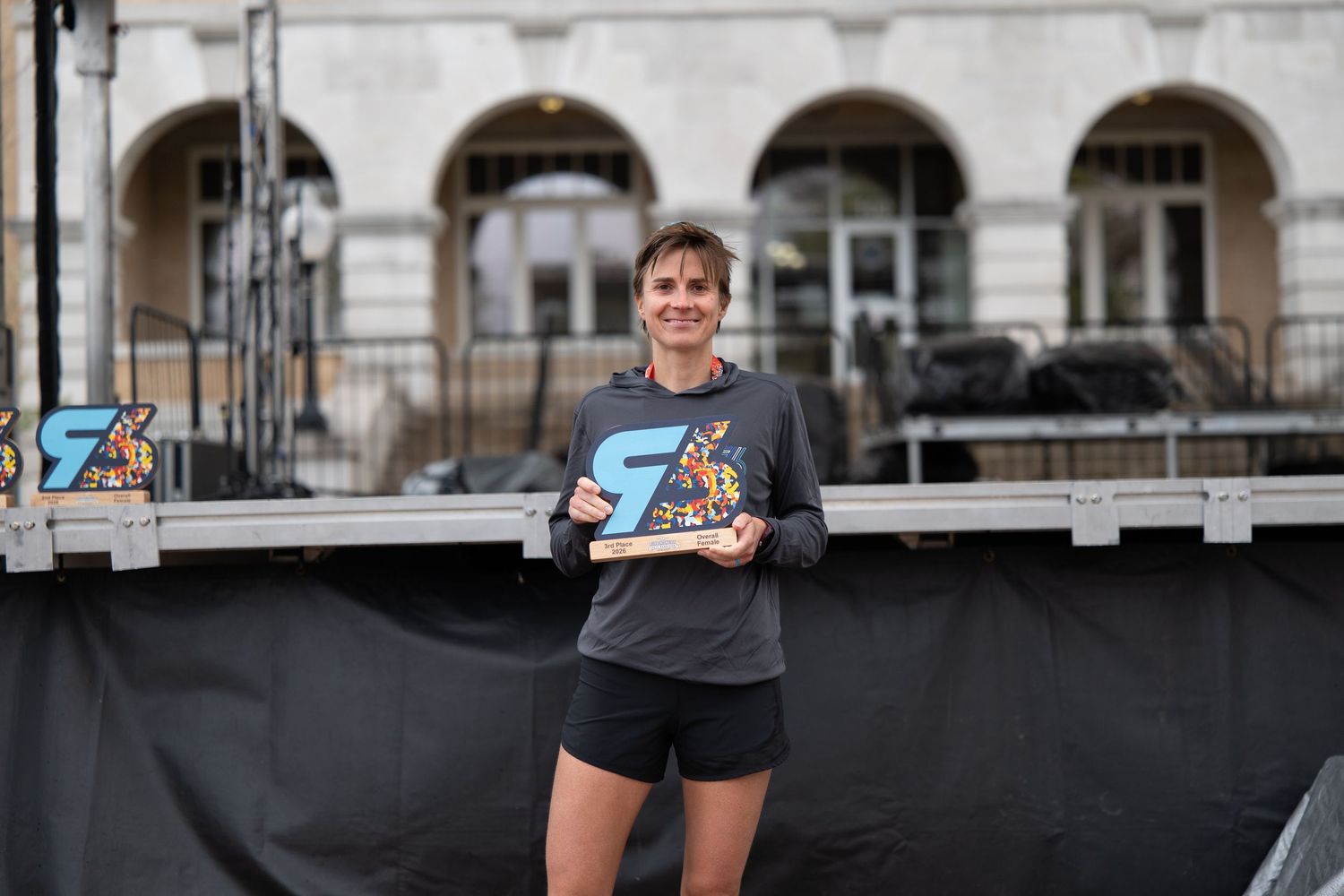 Athlete proudly holds a trophy on an outdoor stage after winning a running race event.