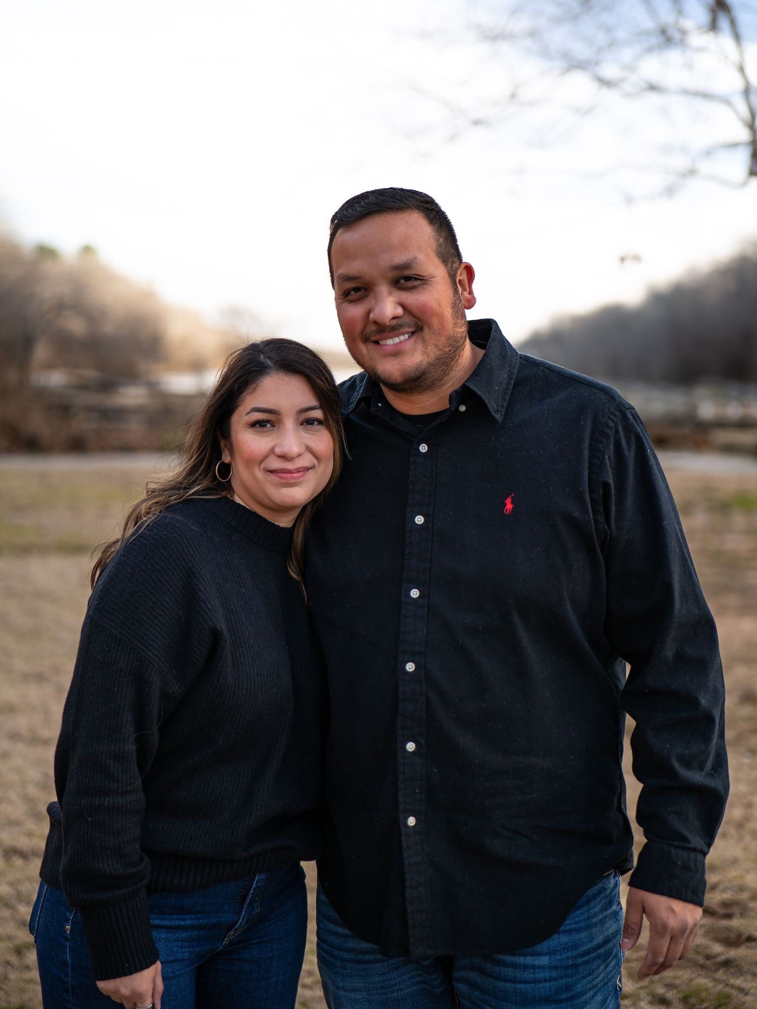 A couple in matching black tops and jeans poses together outdoors during golden hour in a series of casual portraits.
