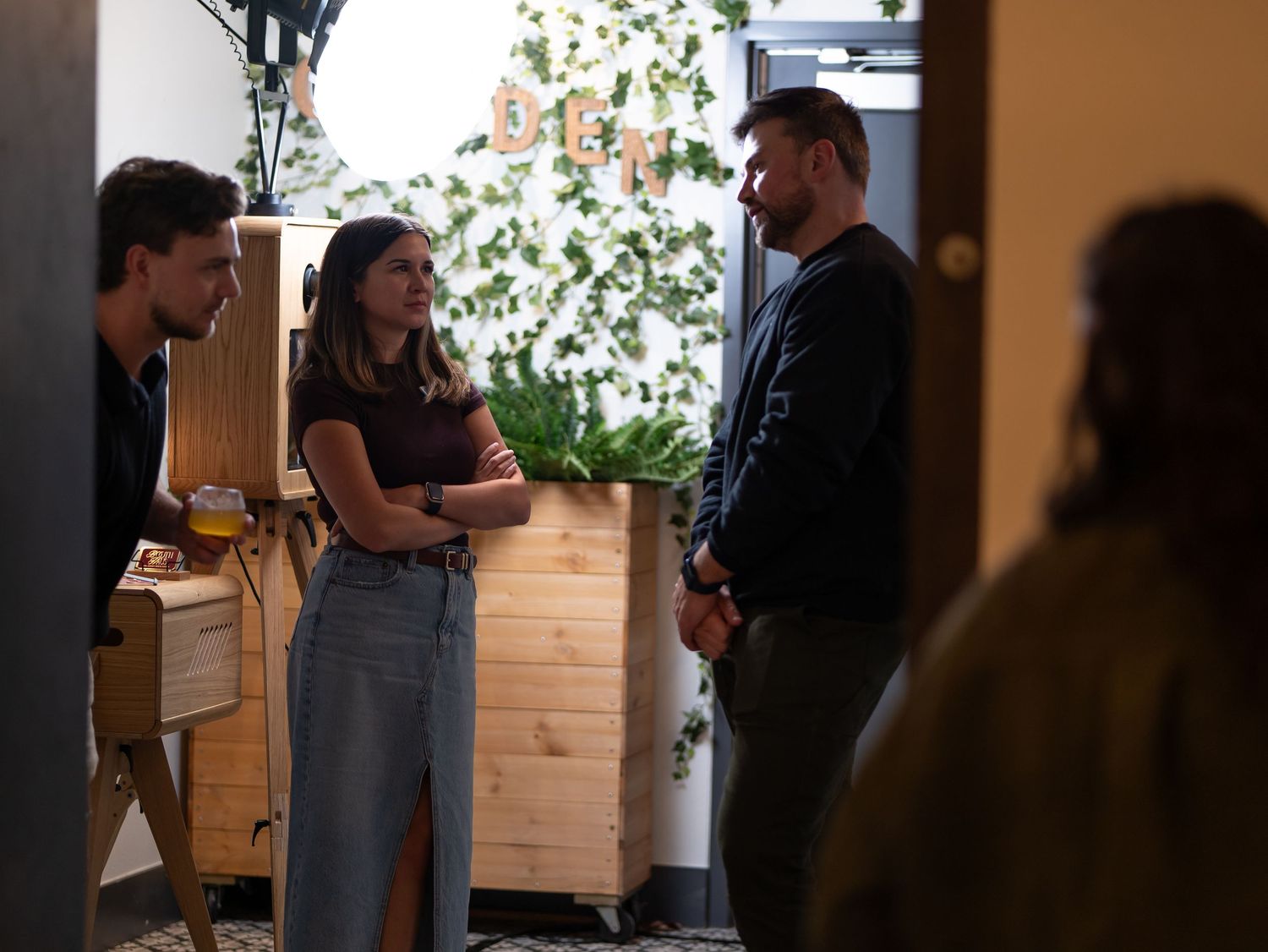 People gathered in conversation at an indoor event with wooden paneled walls and warm lighting.