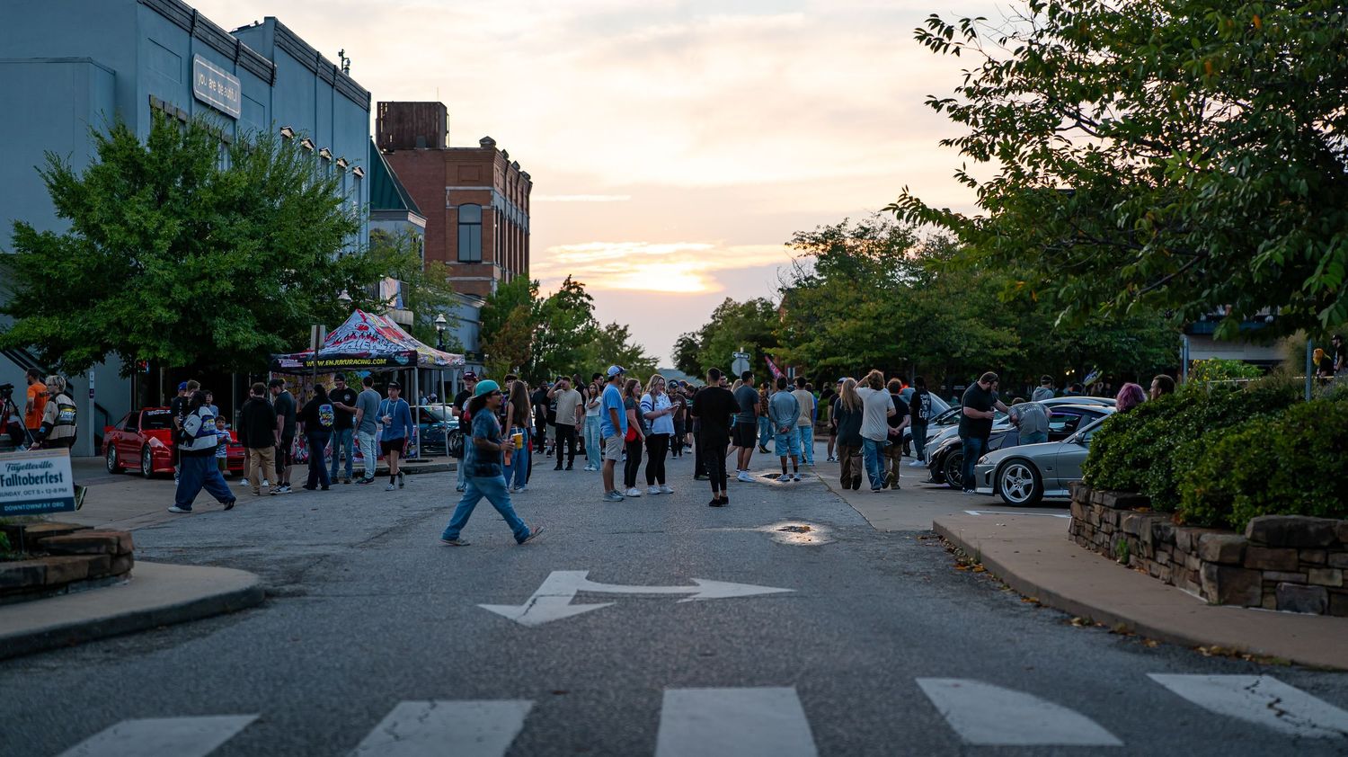 Urban street scene at dusk with brick buildings and pedestrians walking along a sidewalk.